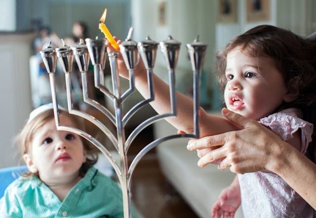 Young girl lights the Hanukkah menorah with help from adult