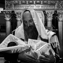 Orthodox Jewish man holding a newborn baby wrapped in a ceremonial blanket during the brit milah circumcision ceremony (Shutterstock) Orthodox Jewish man holding a newborn baby wrapped in a ceremonial blanket during the brit milah circumcision ceremony (Shutterstock)