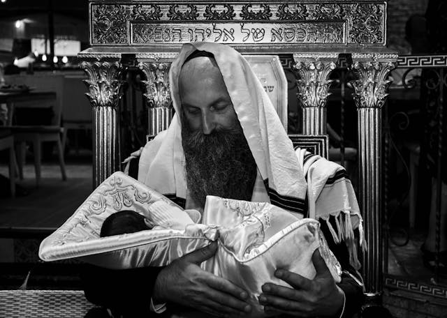 Orthodox Jewish man holding a newborn baby wrapped in a ceremonial blanket during the brit milah circumcision ceremony (Shutterstock) Orthodox Jewish man holding a newborn baby wrapped in a ceremonial blanket during the brit milah circumcision ceremony (Shutterstock)
