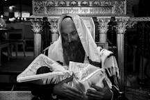 Orthodox Jewish man holding a newborn baby wrapped in a ceremonial blanket during the brit milah circumcision ceremony (Shutterstock)