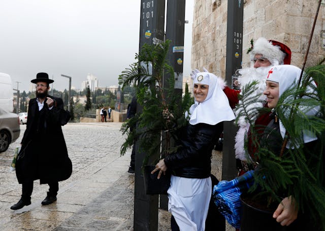A Jewish man walks past a man dressed as Santa Claus and Russian Orthodox nuns in Jerusalem's Old City. (Photo by Gali TIbbon/ AFP via Getty Images.) A Jewish man walks past a man dressed as Santa Claus and Russian Orthodox nuns in Jerusalem's Old City. (Photo by Gali TIbbon/ AFP via Getty Images.)