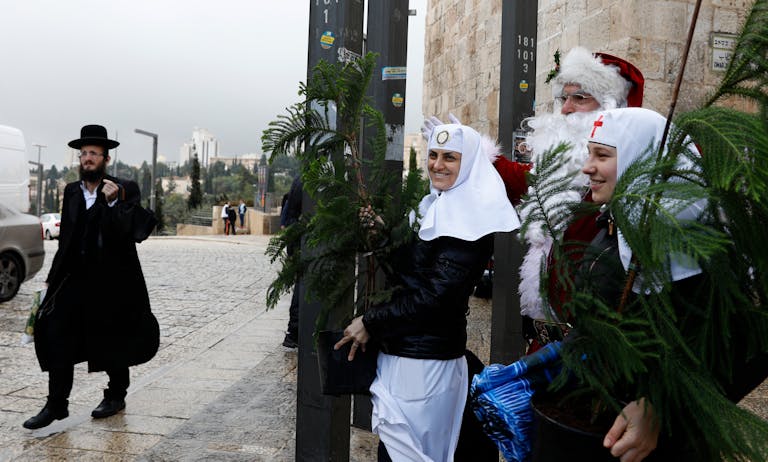 A Jewish man walks past a man dressed as Santa Claus and Russian Orthodox nuns in Jerusalem's Old City. (Photo by Gali TIbbon/ AFP via Getty Images.) A Jewish man walks past a man dressed as Santa Claus and Russian Orthodox nuns in Jerusalem's Old City. (Photo by Gali TIbbon/ AFP via Getty Images.)