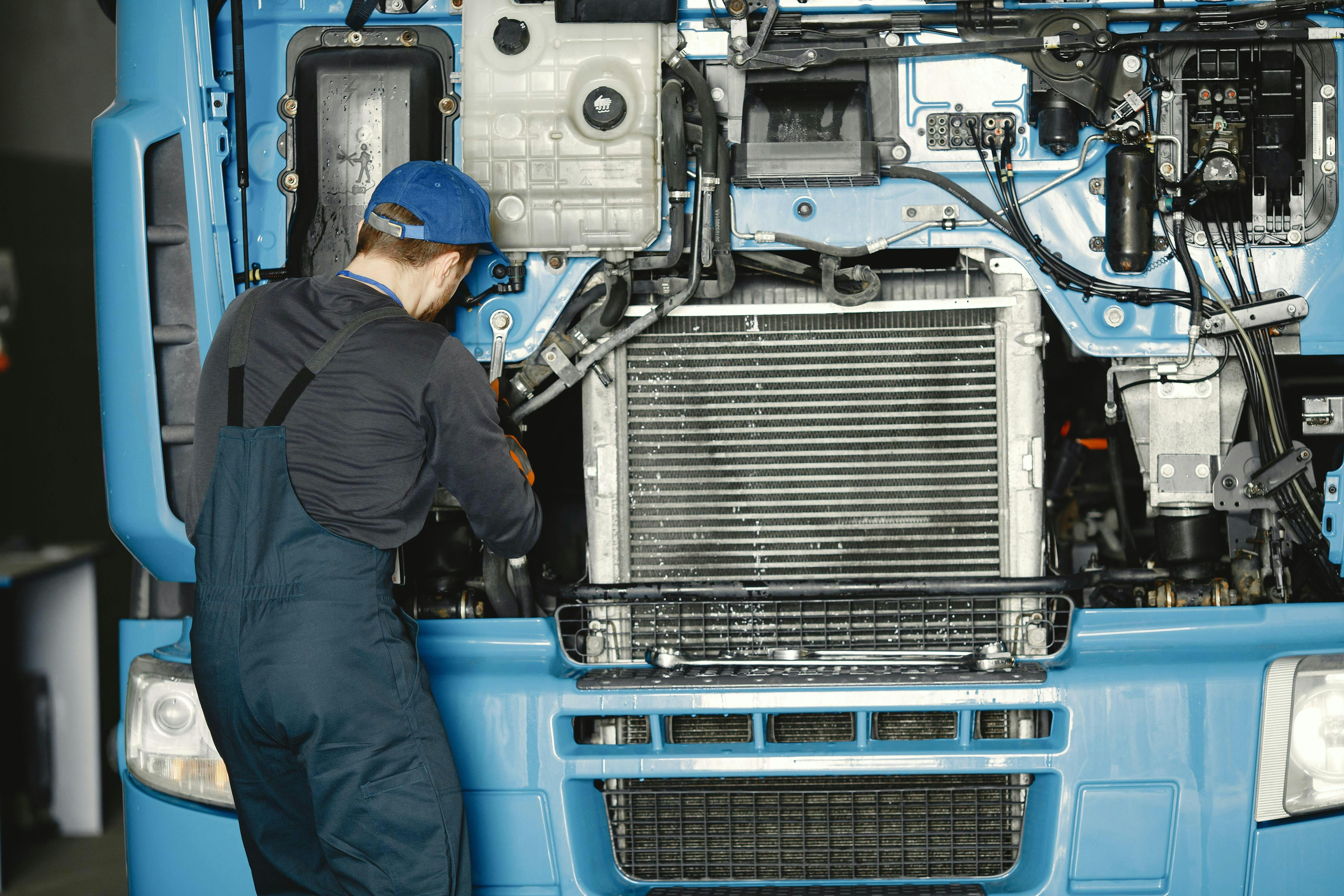 Technieker voert onderhoud uit aan de radiator en het motorkoelsysteem van een moderne vrachtwagen in een professionele werkplaats.