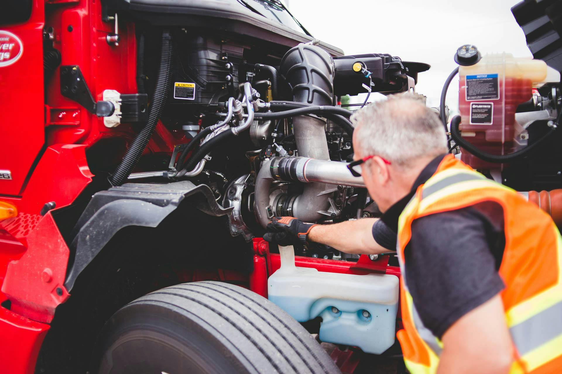 Monteur controleert onderdelen van het motorkoelsysteem, waaronder koelvloeistofreservoir, slangen en motorcomponenten van een vrachtwagen.