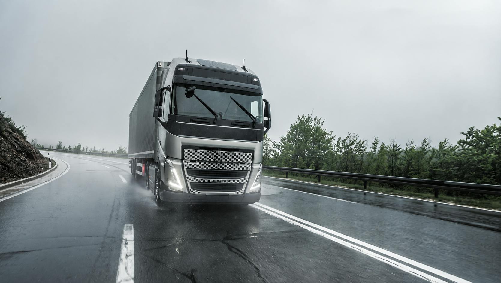 Europese vrachtwagen rijdt over een natte snelweg in de regen met actieve ruitenwissers.