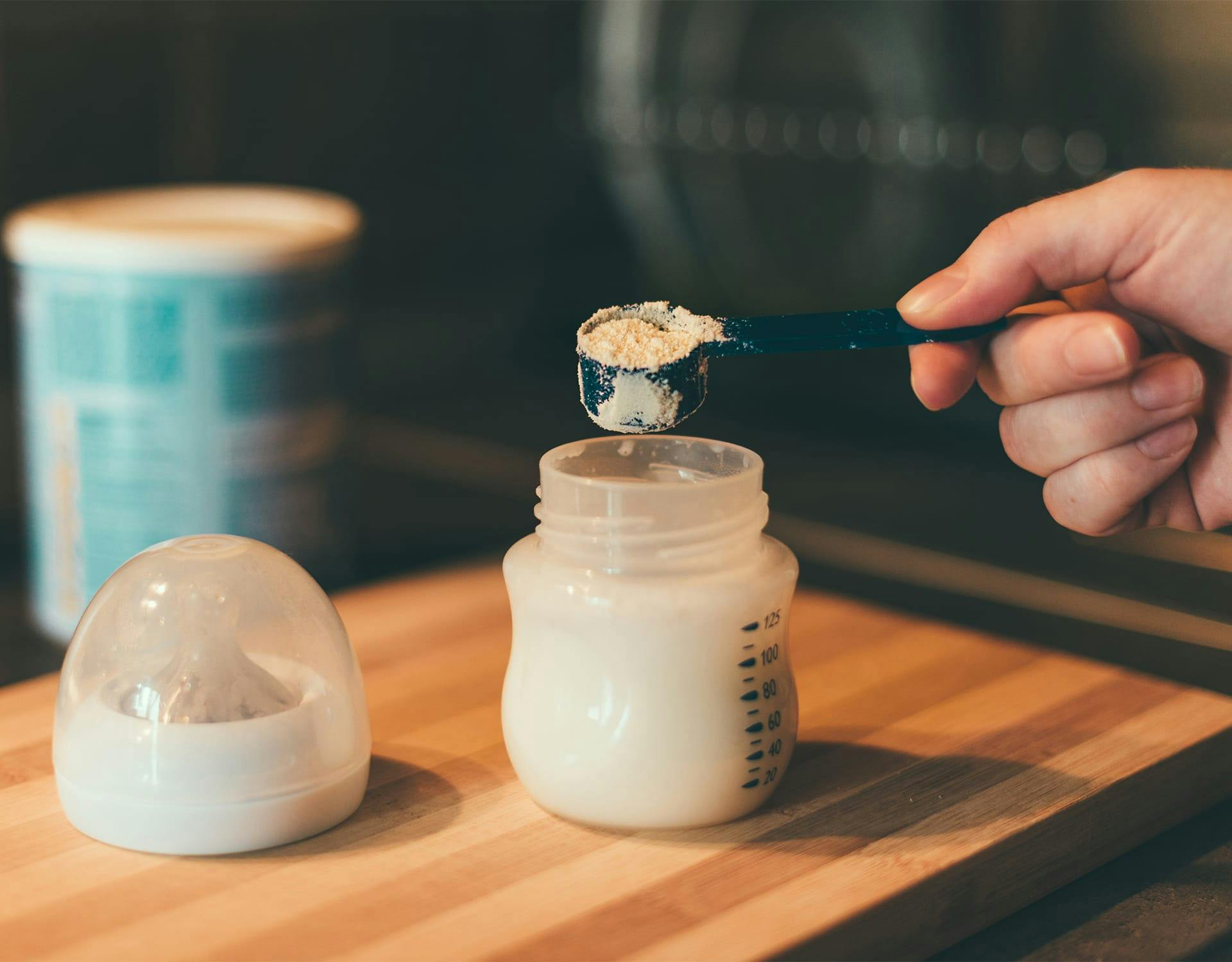 person pouring powder into a baby bottle