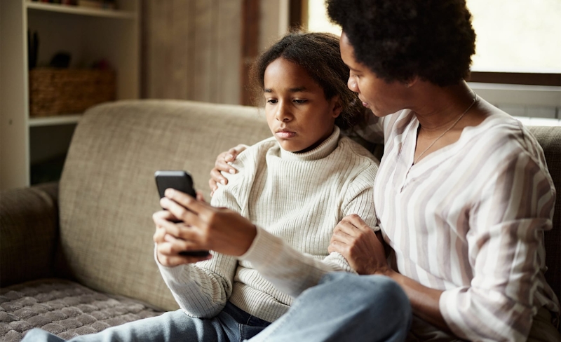 mother hugging daughter while shes on her phone