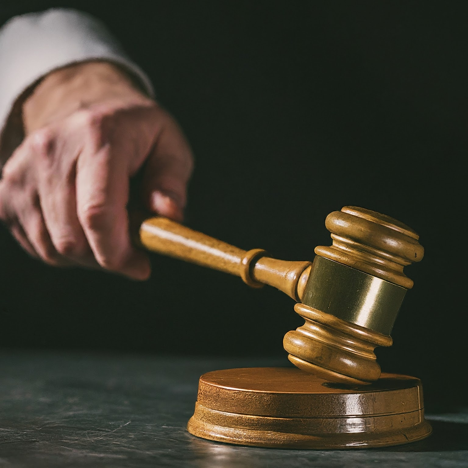 This image shows a judge's hand hitting a wooden gavel on a block. 