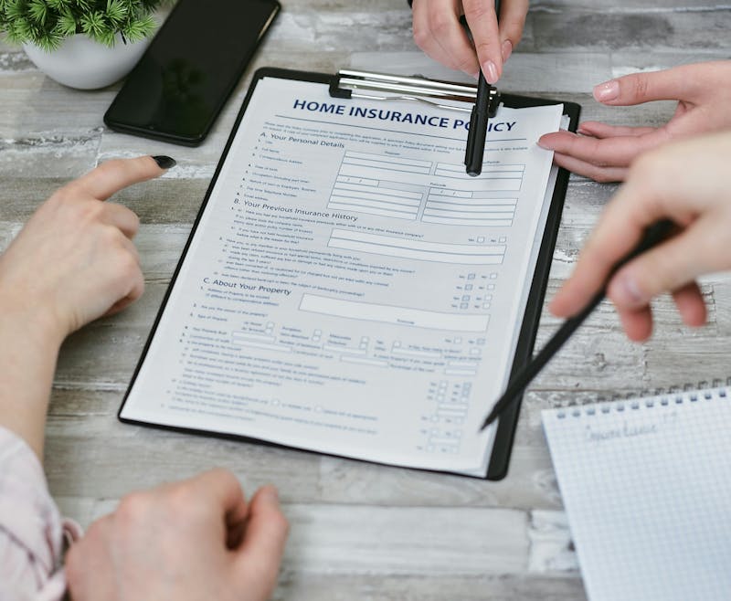 A group of people discussing and pointing at a home insurance policy document on a clipboard, with a smartphone and notepad on a wooden table.
