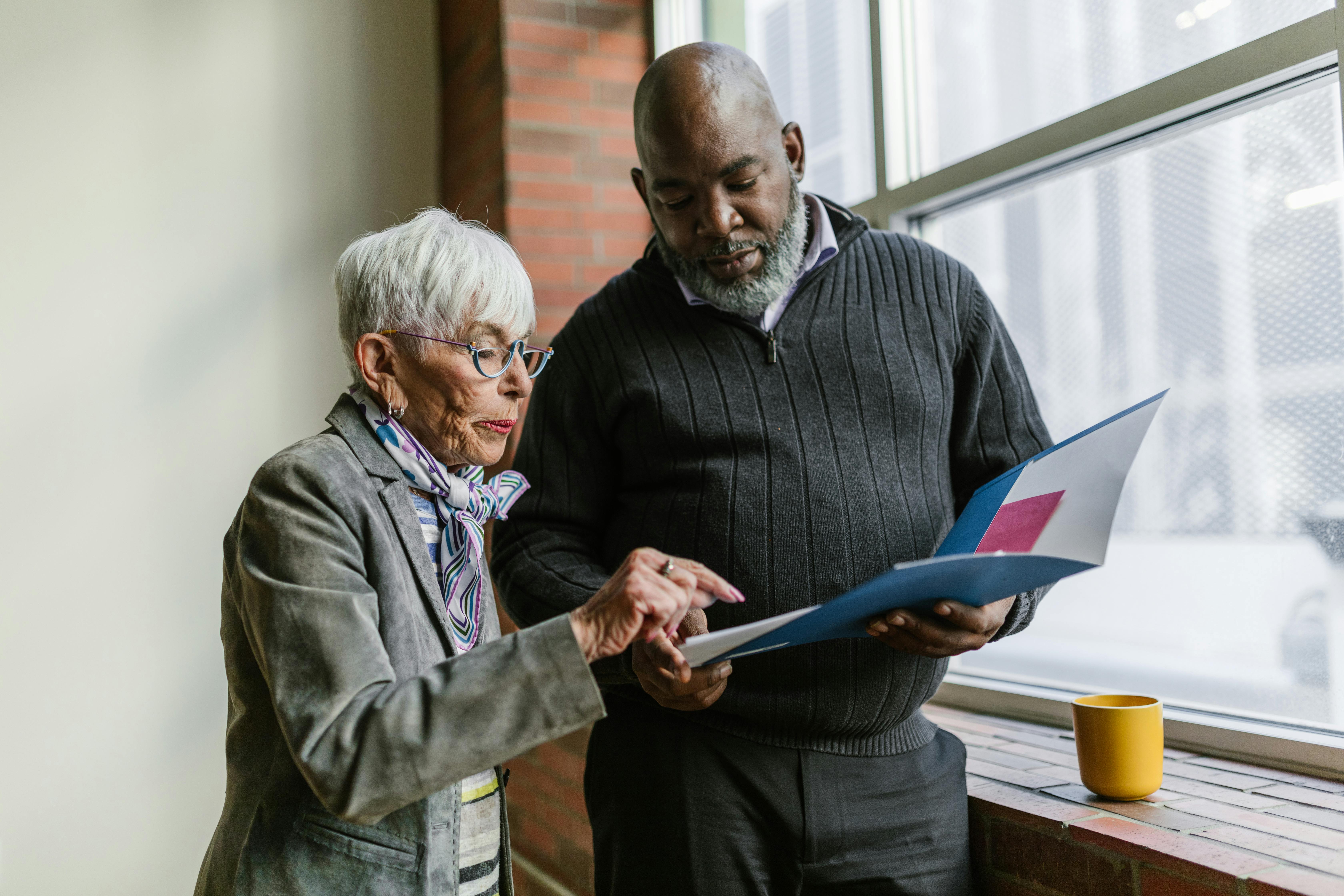 Two people are looking at papers together. The woman is pointing at something, and the man is holding the folder. They look like they’re working on something important.