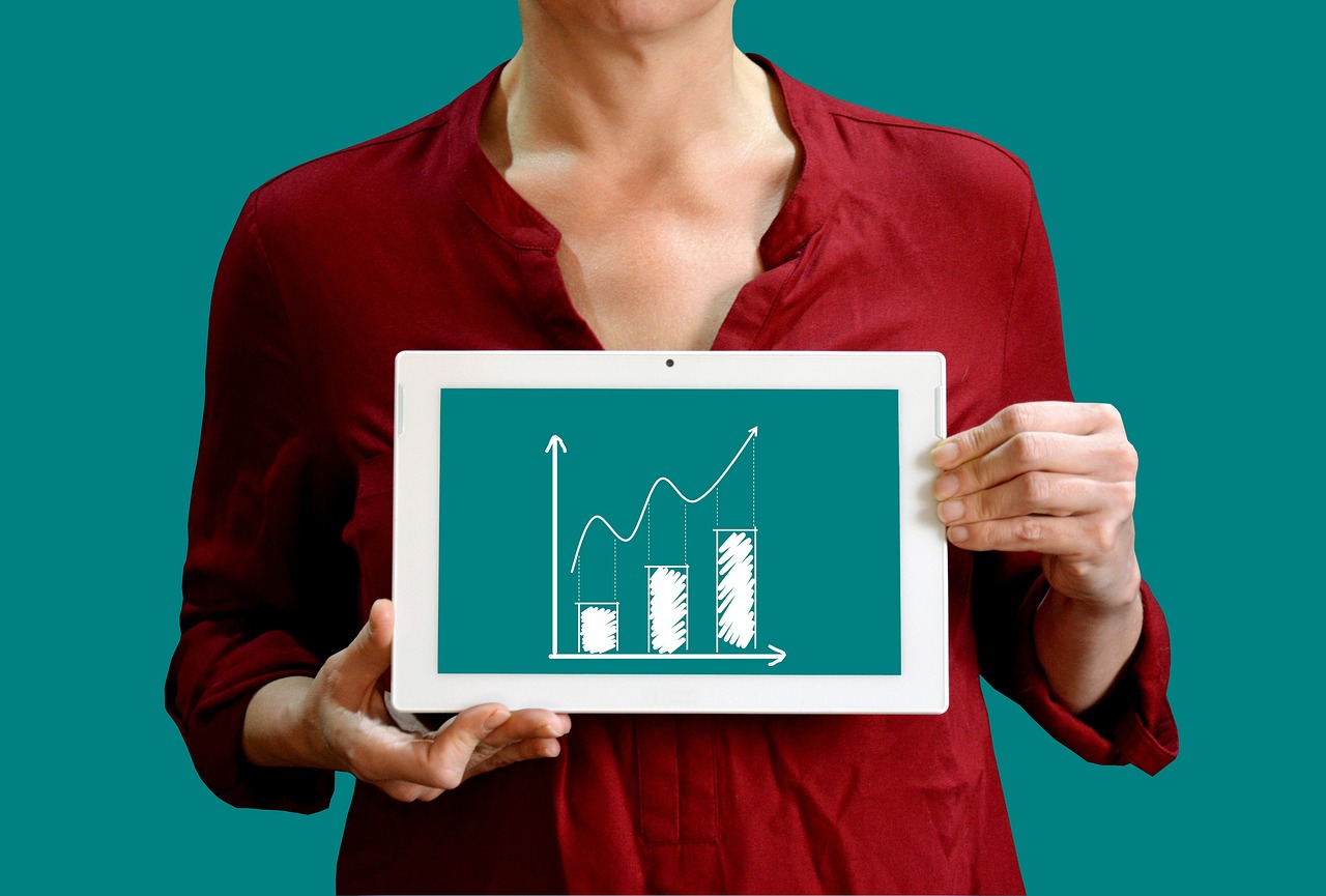 Person in a red shirt holding a tablet showing a rising bar graph with an upward trend.