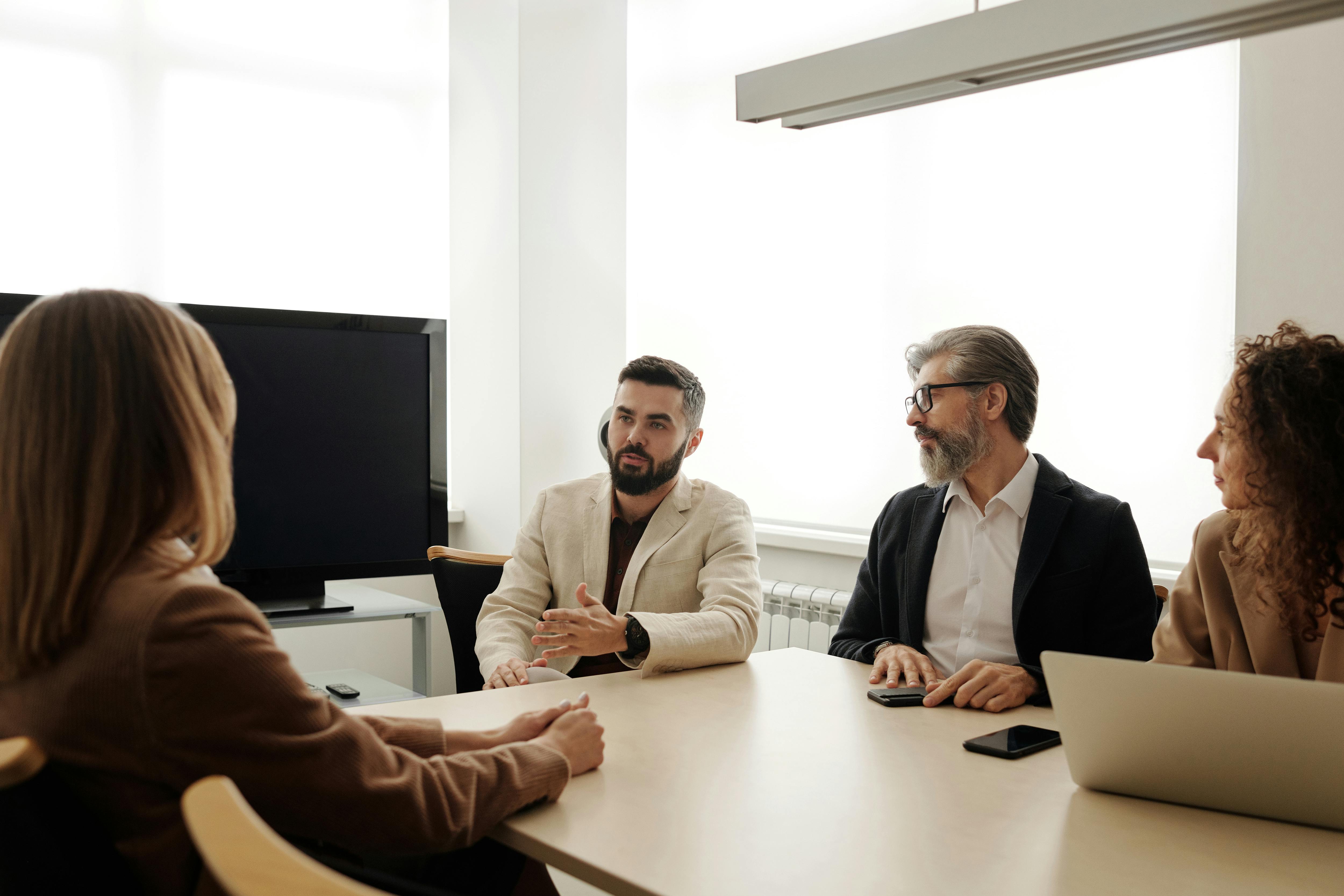 Four professionals in a meeting discussing business at a conference table.