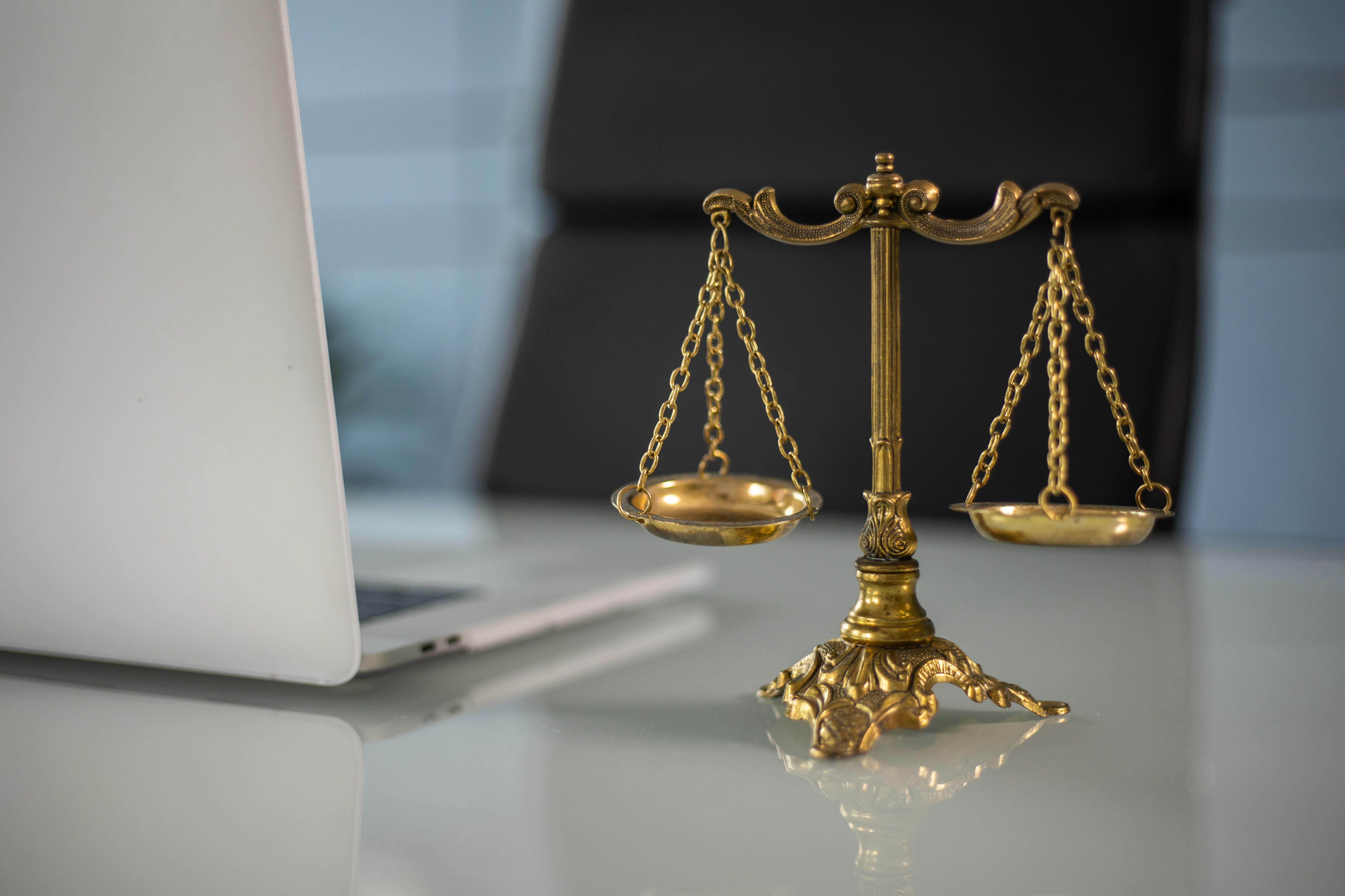 Golden scales of justice placed on a desk beside a laptop.