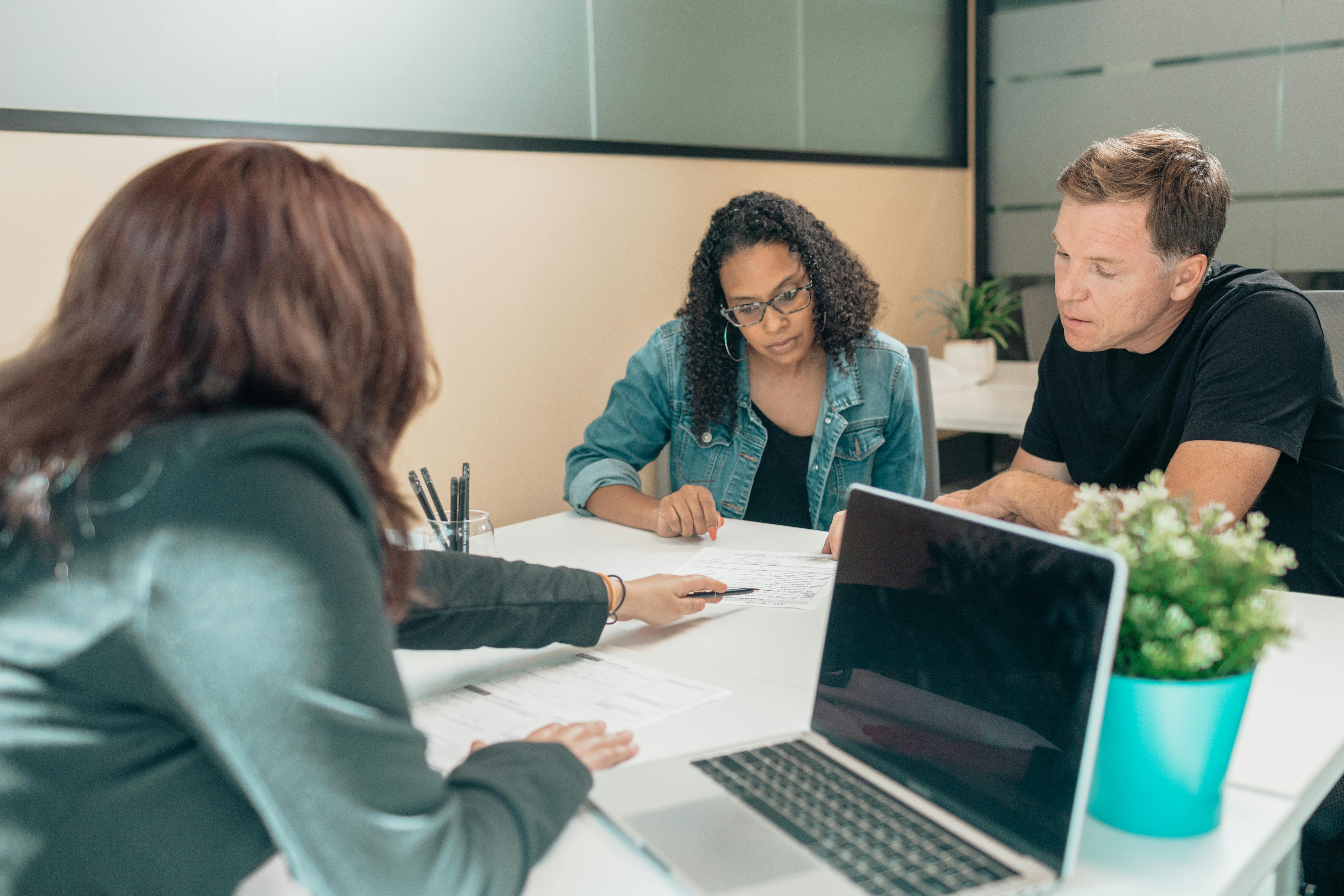 Three people sitting at a desk in an office, reviewing and discussing documents together.