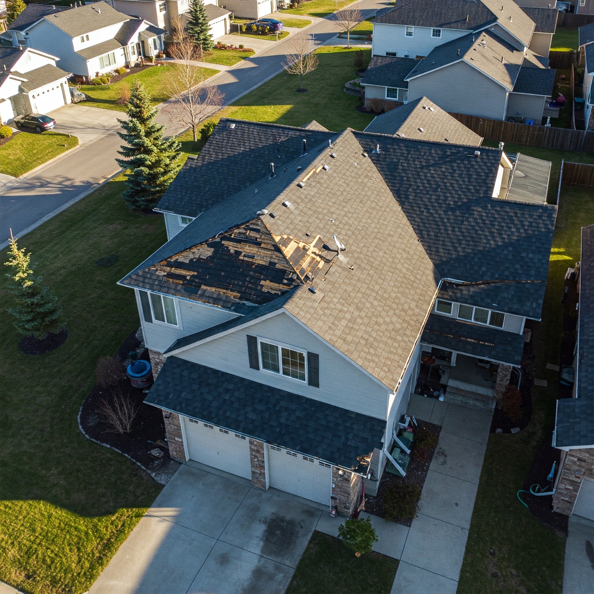 Aerial view of a house with missing shingles showing roof damage in a suburban neighborhood.