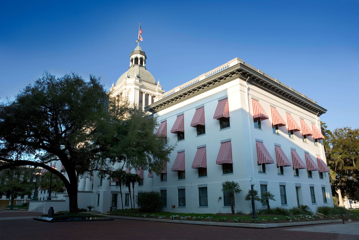 The Florida State Capitol building with red and white striped window awnings and a U.S. flag on top.