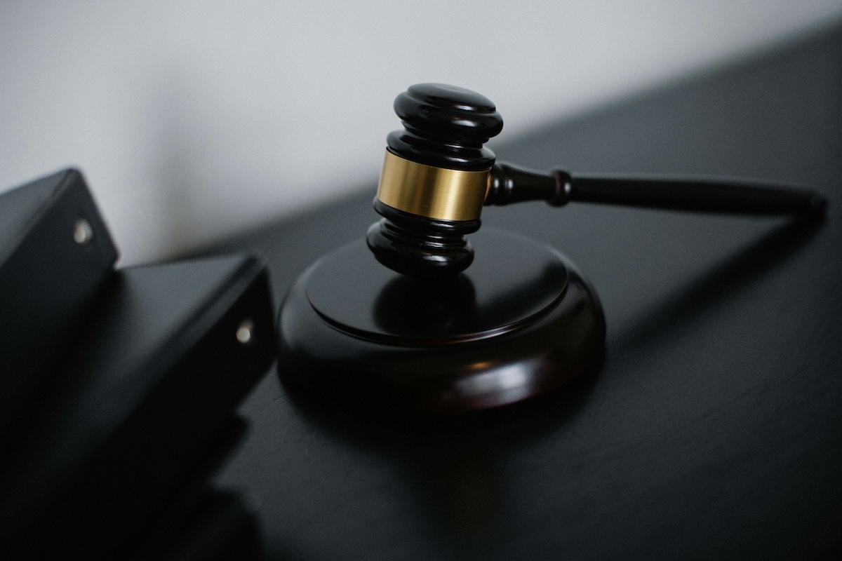 A judge's gavel resting on a sound block next to black folders on a dark desk.