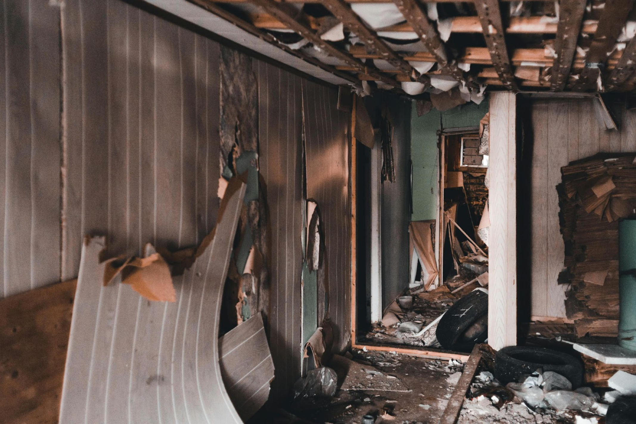 A damaged interior hallway with debris, broken walls, and a partially collapsed ceiling, showing signs of severe property destruction.