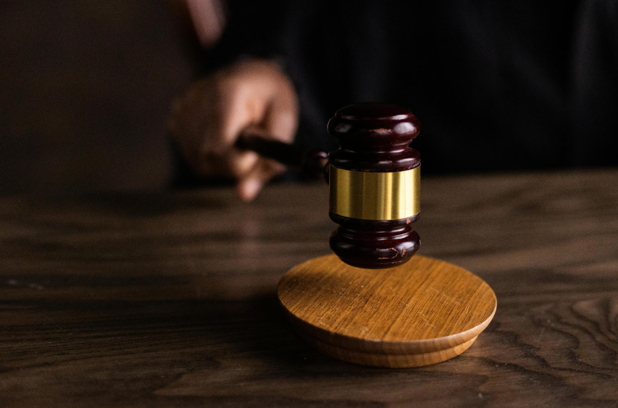  &bull; A judge's hand is seen holding a gavel, about to strike a wooden sound block in a courtroom setting.
