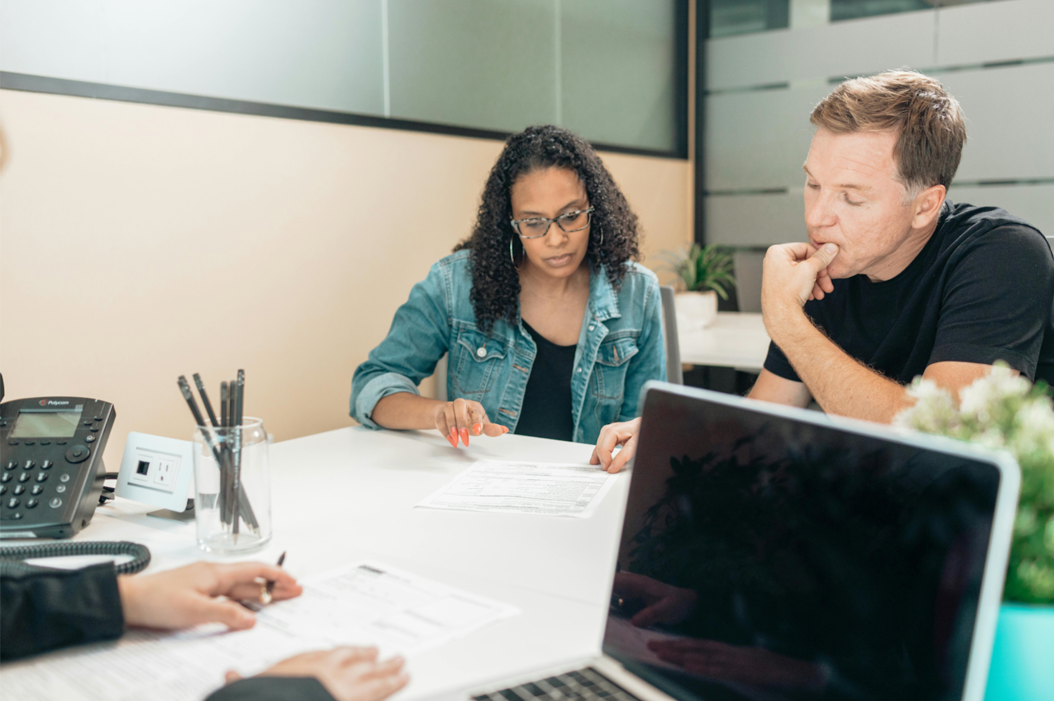A person is filling out paperwork at a desk, while another couple sits&nbsp;across holding hands, possibly during a consultation or legal meeting.