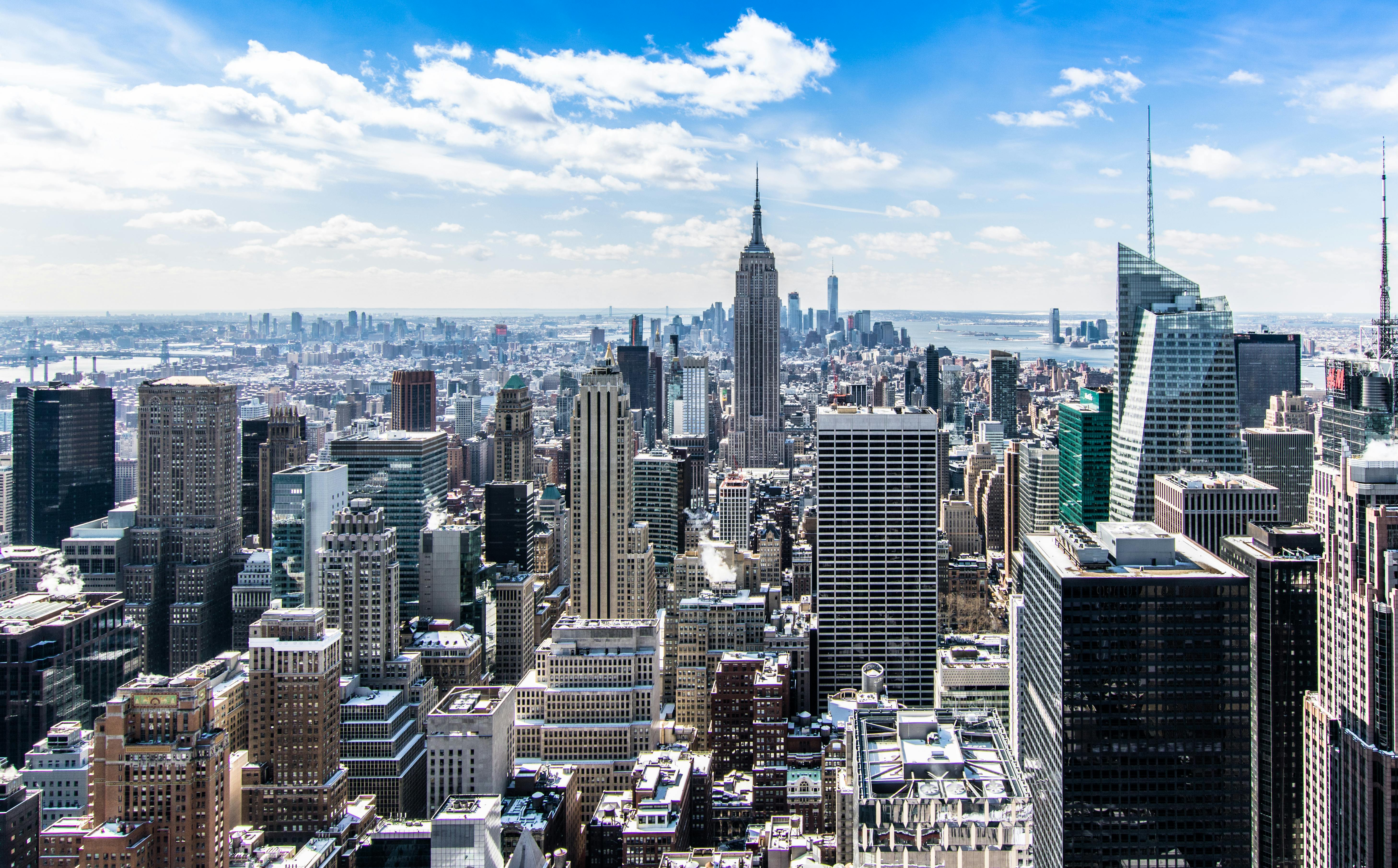 Aerial view of New York City with tall skyscrapers under a bright blue sky.