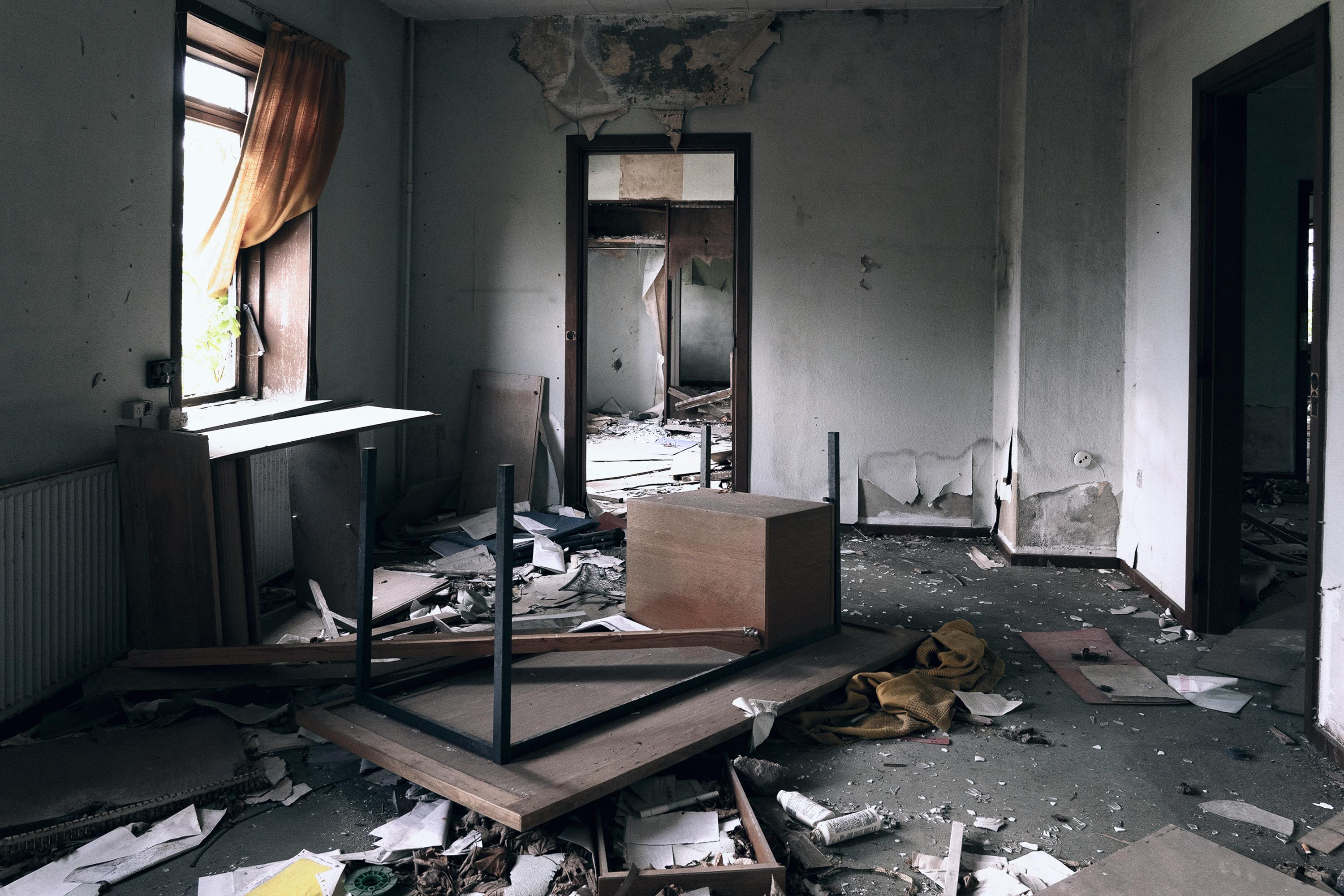 A damaged room with broken furniture, peeling walls, and debris scattered across the floor.