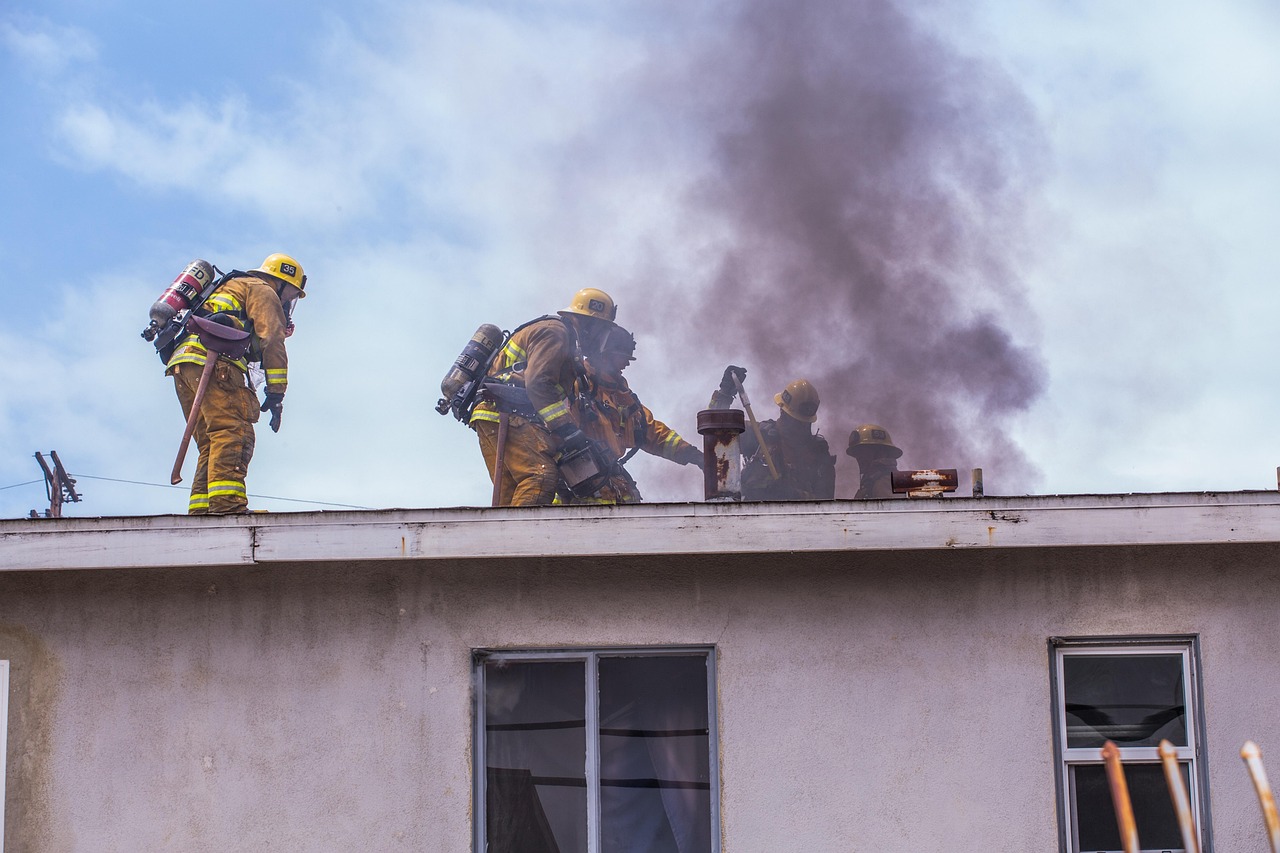 Firefighters on the roof of a building working to control smoke coming from a vent, wearing full gear and oxygen tanks.
