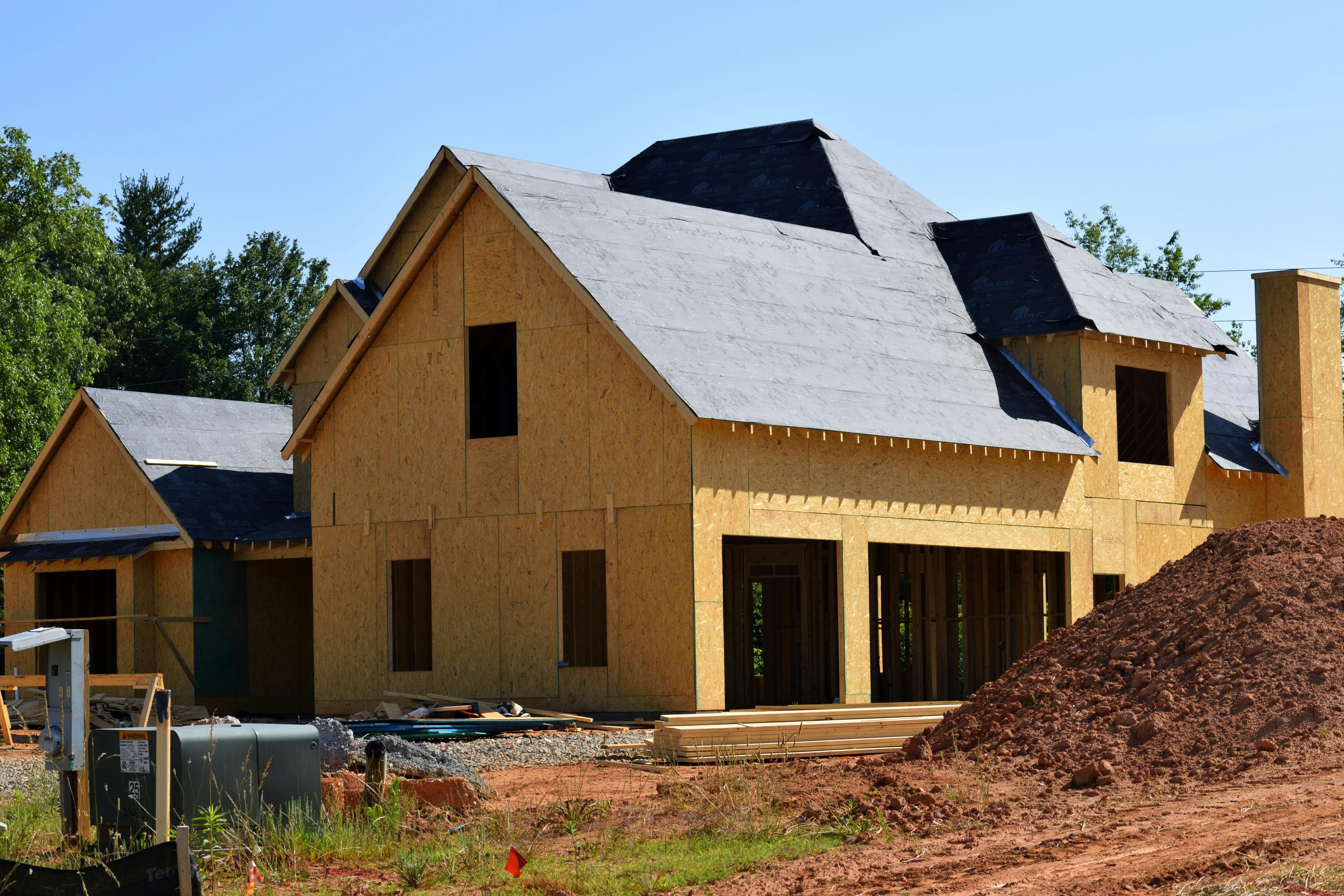 Partially built house with exposed plywood and roofing underlayment at a construction site.