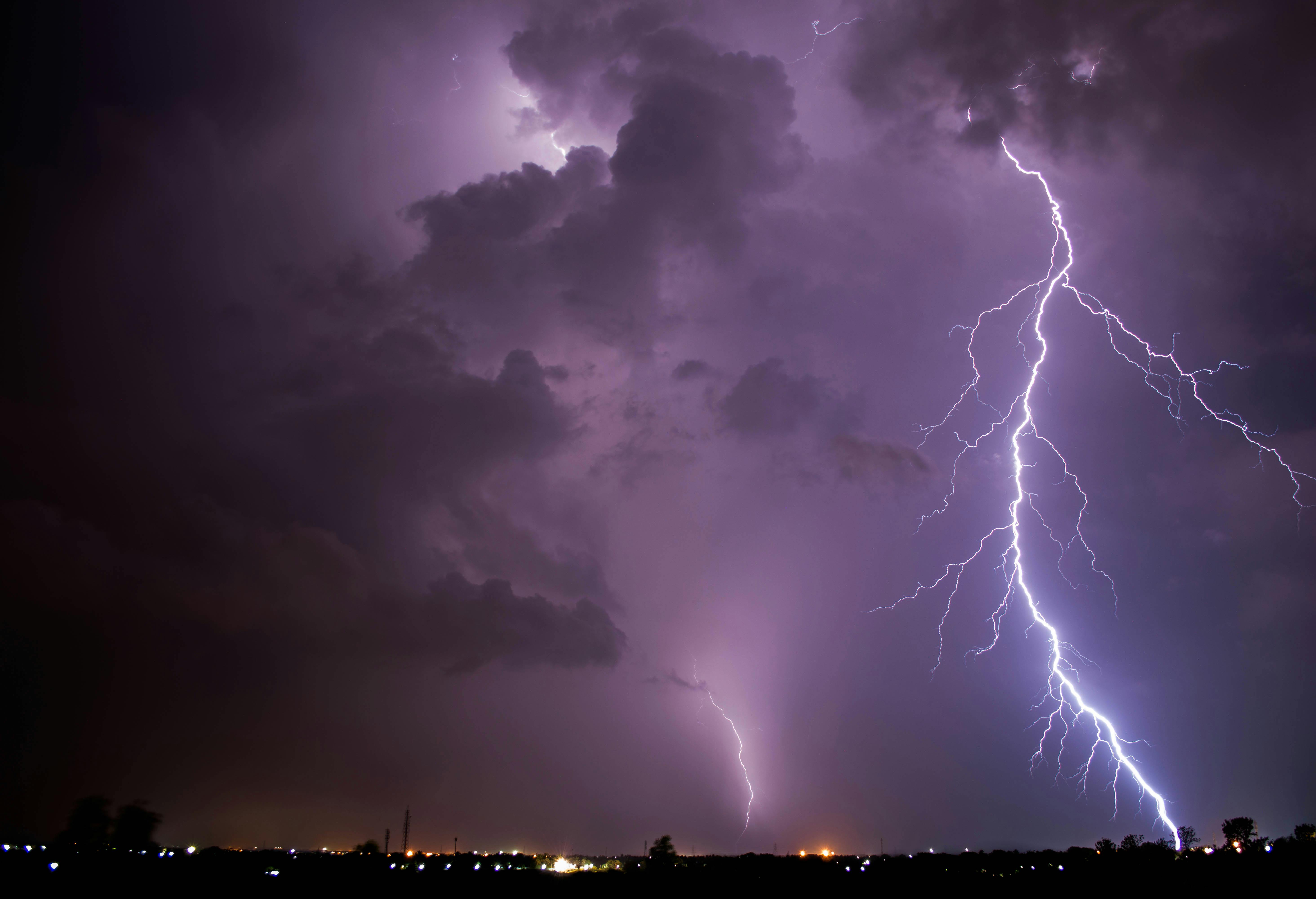 A lightning bolt strikes from a glowing thundercloud against the dark night sky.