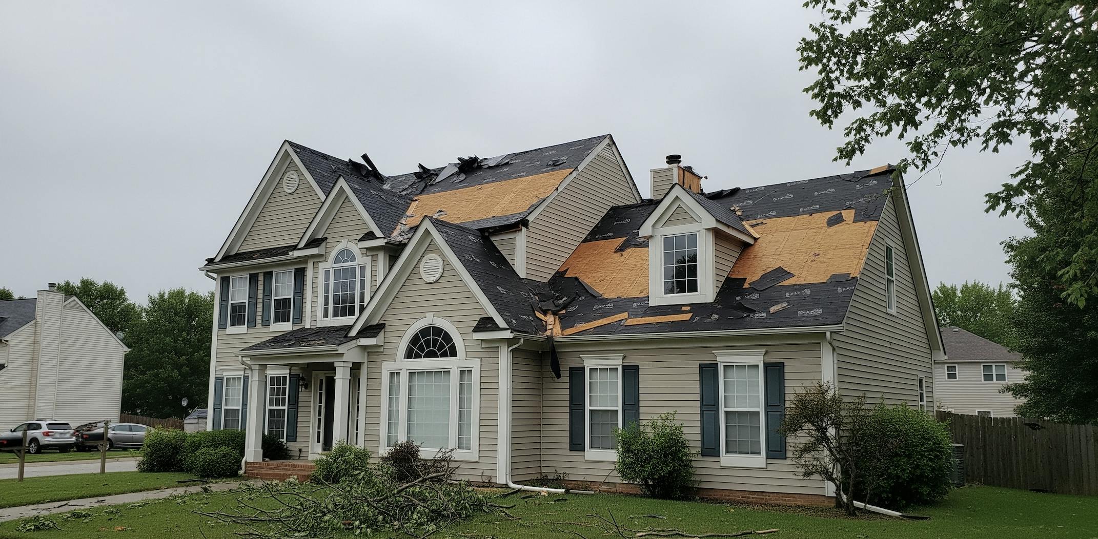 House with severe roof damage; missing shingles and exposed wood after a storm.
