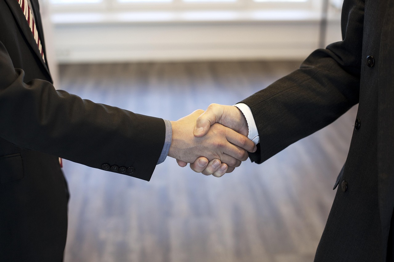 Two people in business suits shaking hands in a professional setting.