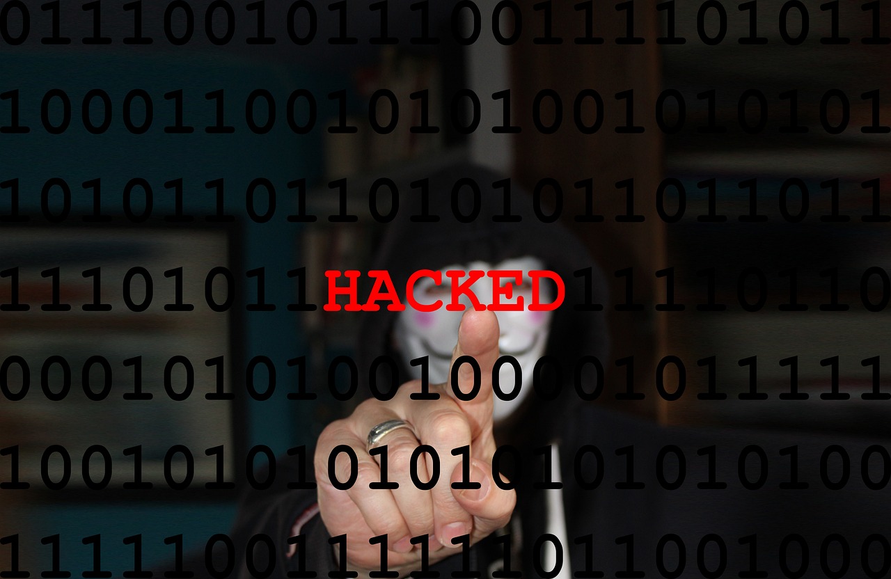 Hacker in mask pointing with the word “HACKED” in red text