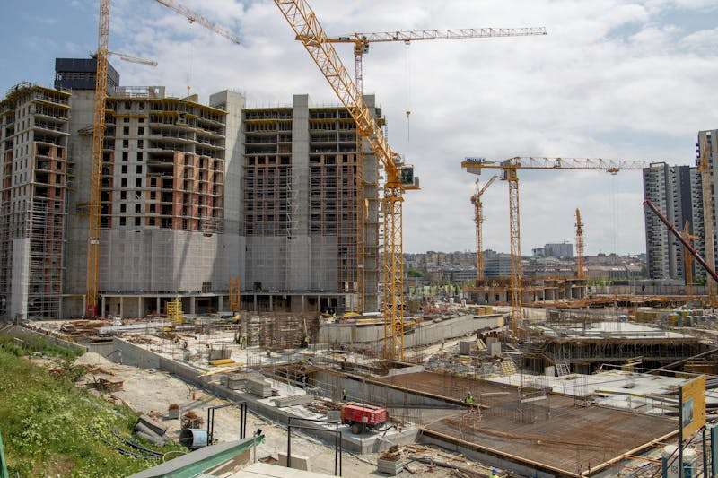 A modern circular building under construction with scaffolding and cranes against a bright blue sky.