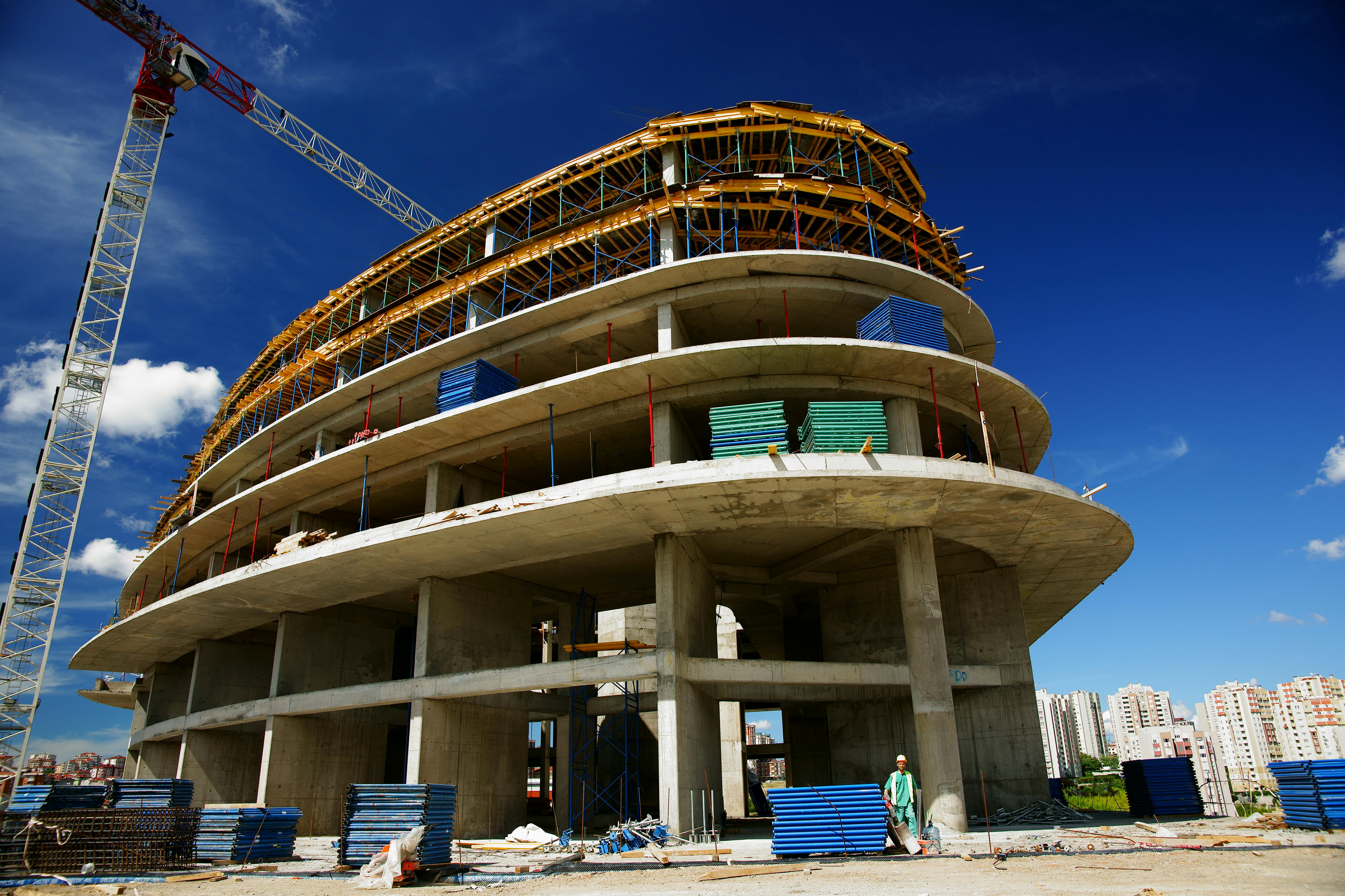 A modern circular building under construction with scaffolding and cranes against a bright blue sky.