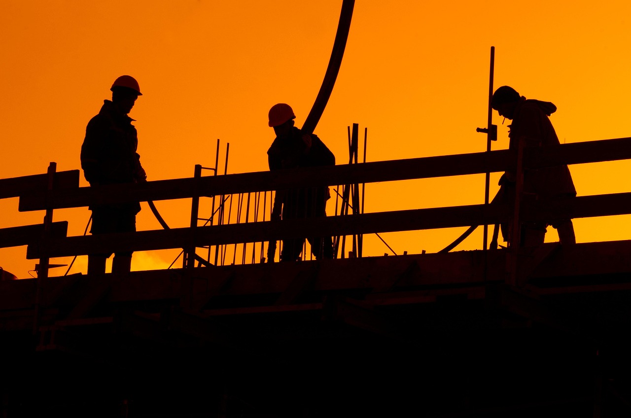 Line of construction workers on a building site at sunset, with an orange sky in the background.