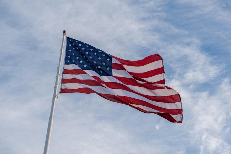 The United States flag waving in the wind against a blue sky with light clouds.