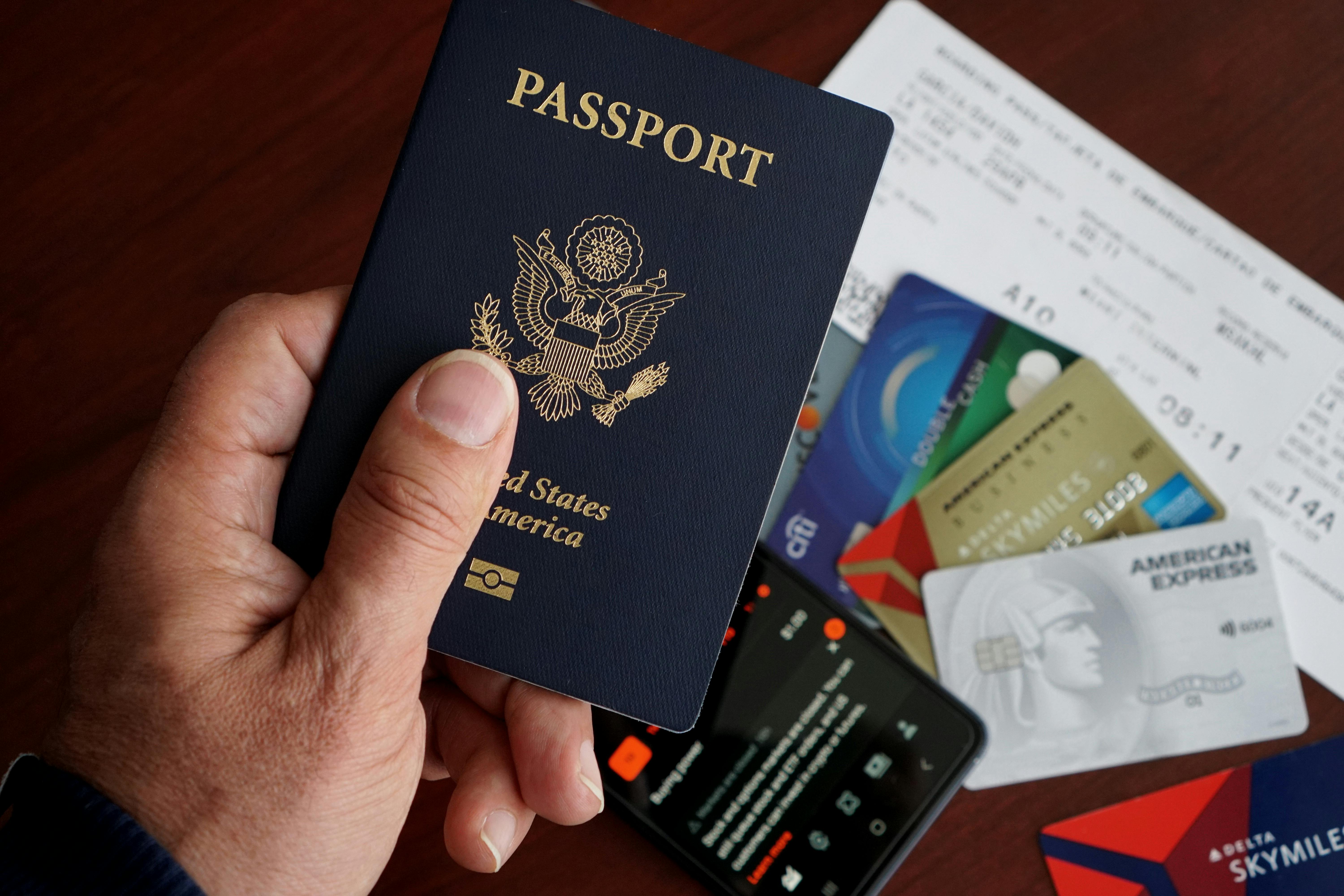A person holds a U.S. passport over a table with credit cards, a boarding pass, and a smartphone.