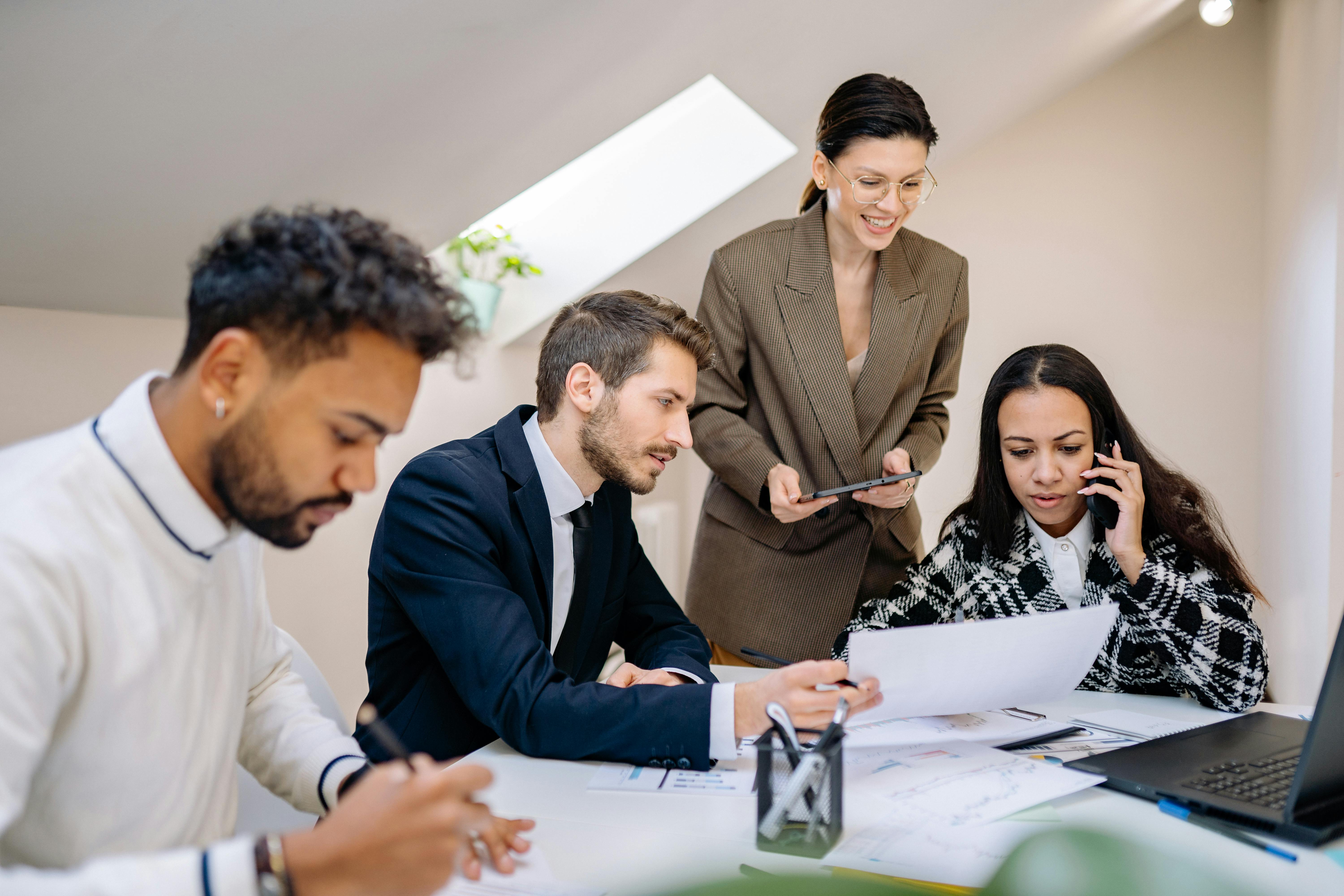 A group of young professionals working together at a table with documents, a laptop, and a phone during a business meeting.