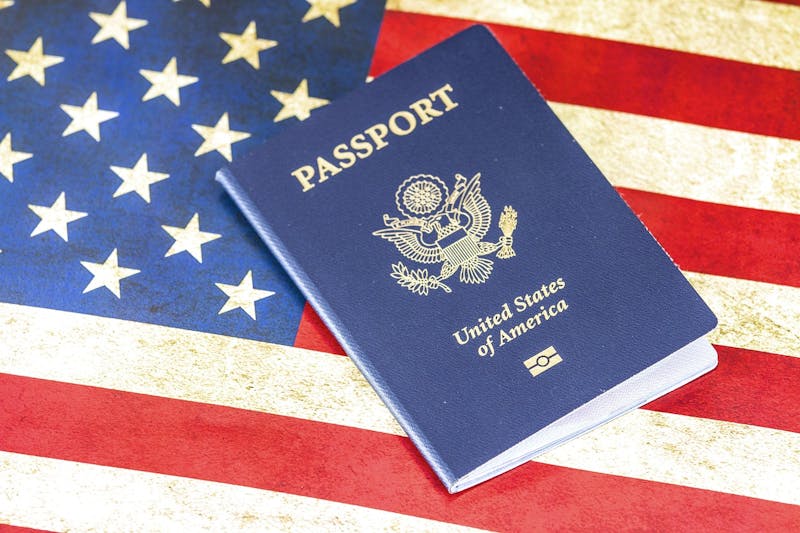 A U.S. passport rests on top of an American flag, symbolizing immigration, travel, or citizenship.