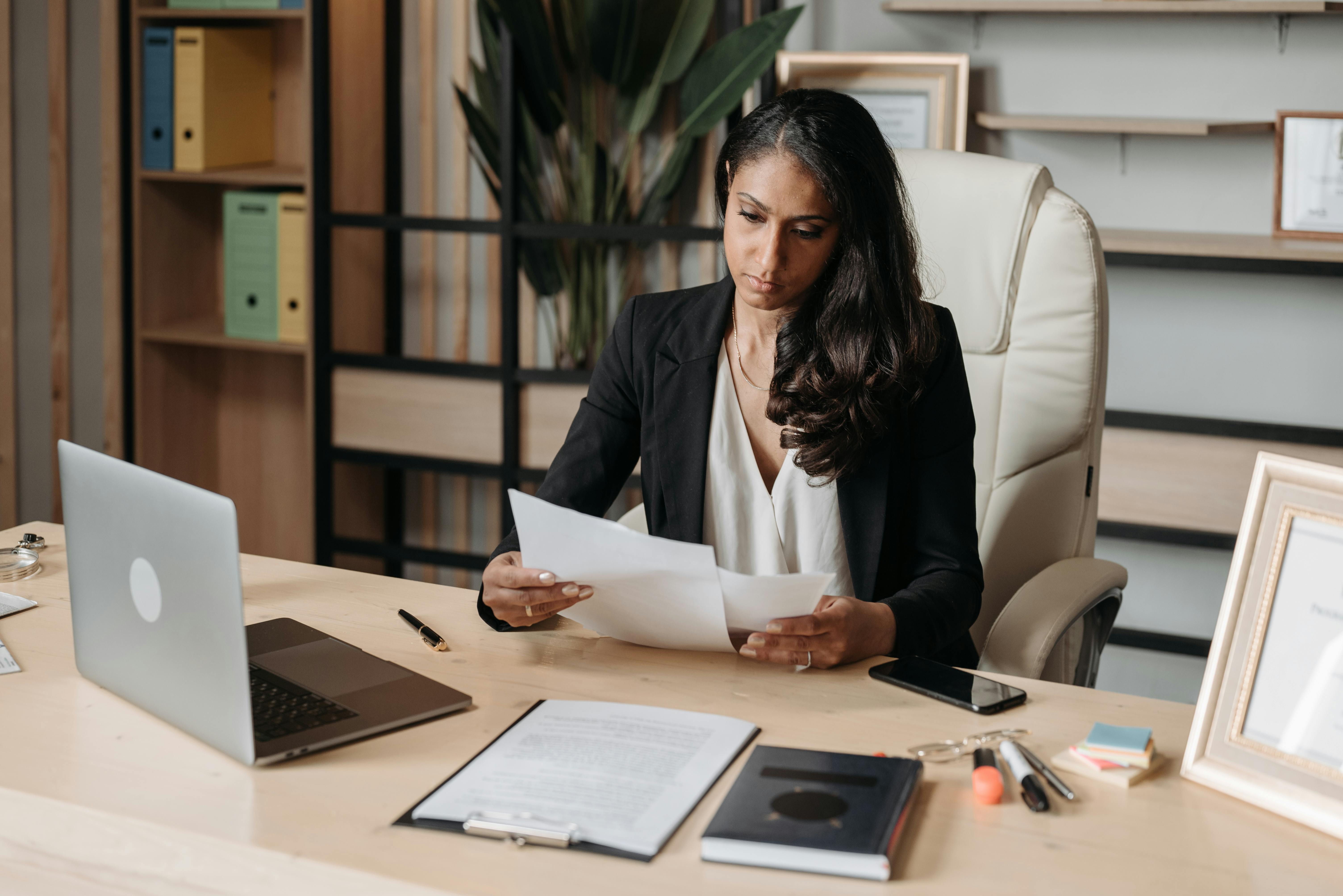 Female attorney sitting at her desk reviewing legal documents, with a laptop, clipboard, and office supplies in front of her