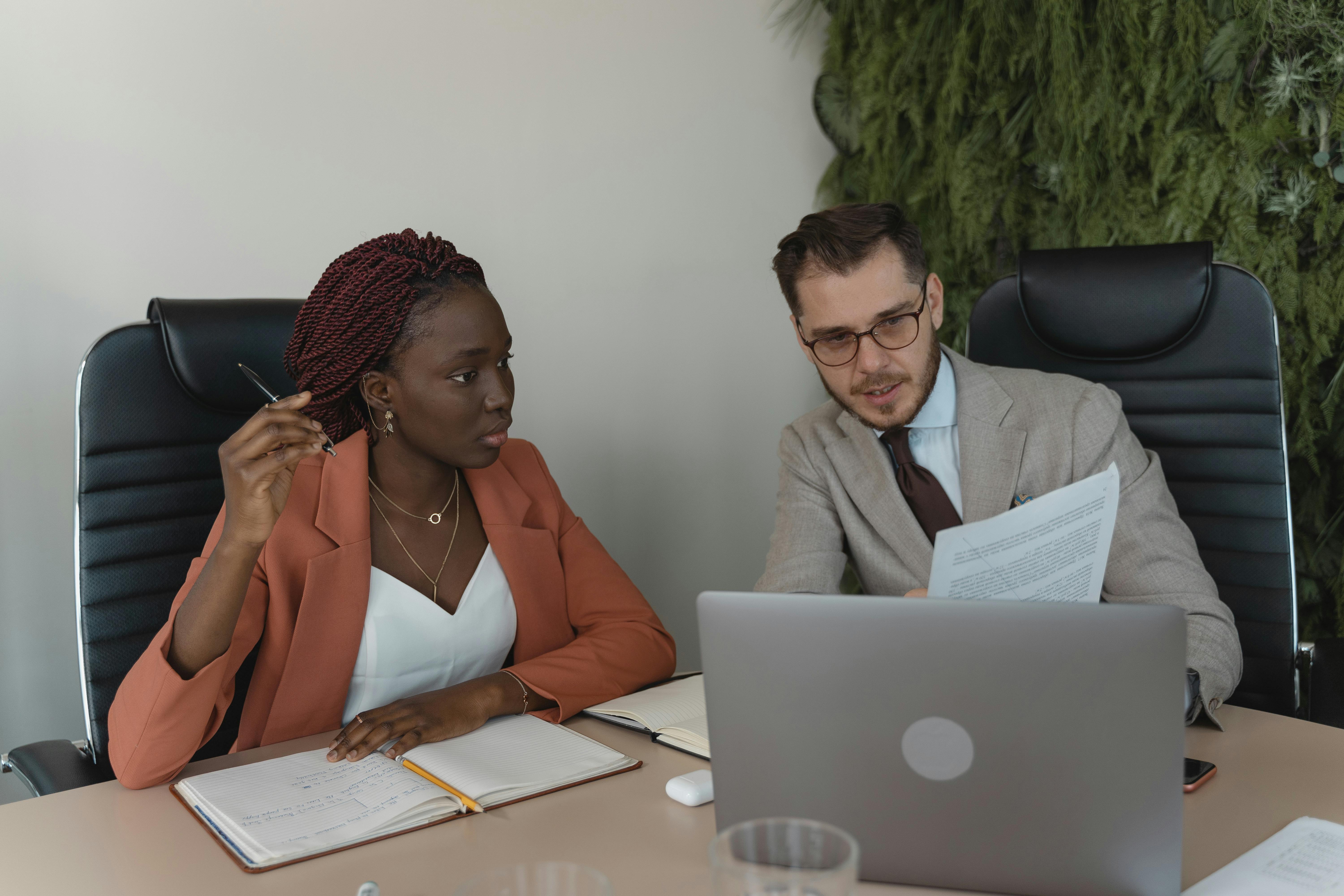Woman and Man reviewing documents together at a desk with a laptop and notebook