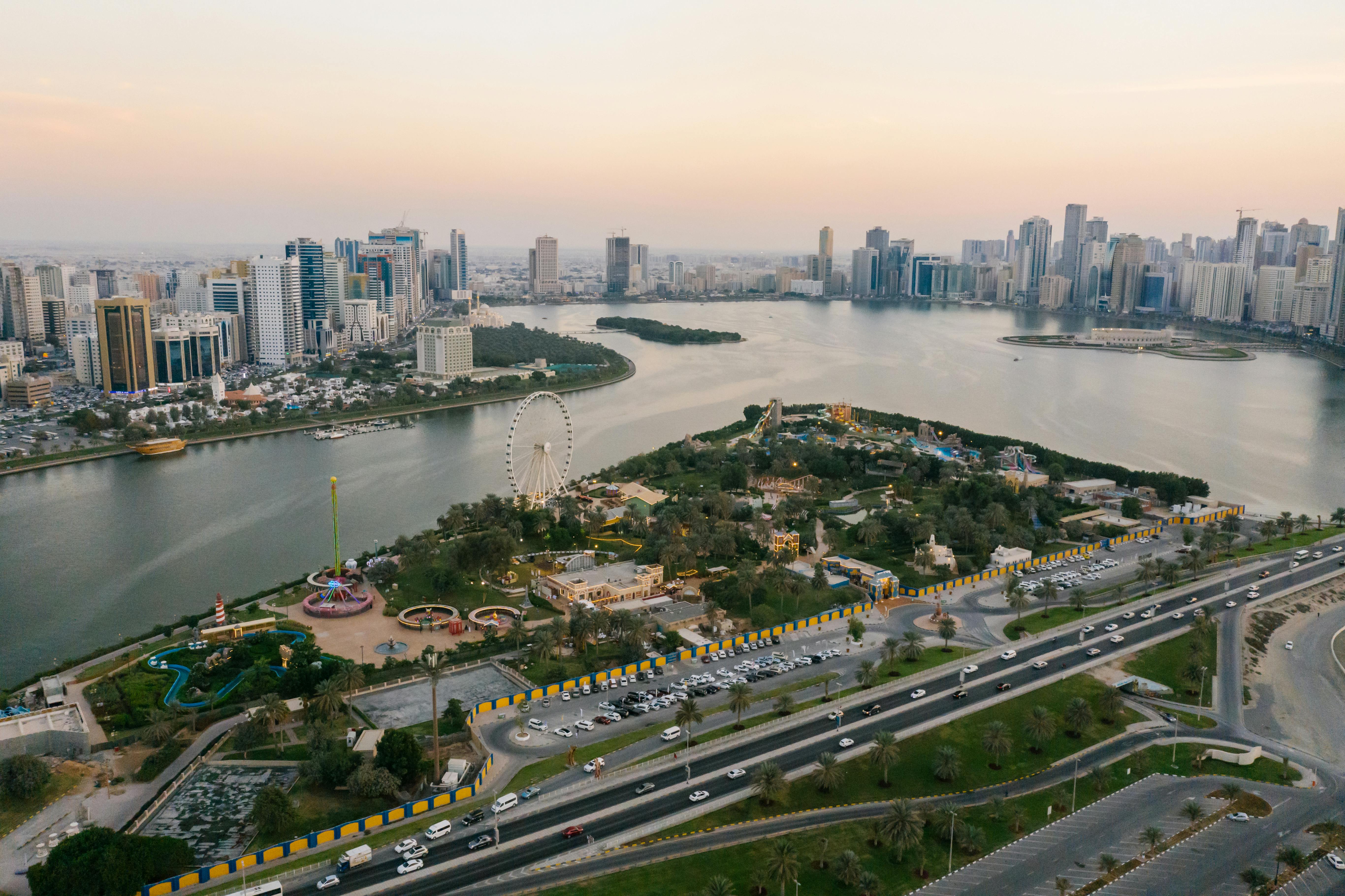 Aerial view of Miami along a waterfront with a Ferris wheel, highways, and high-rise buildings at sunset.