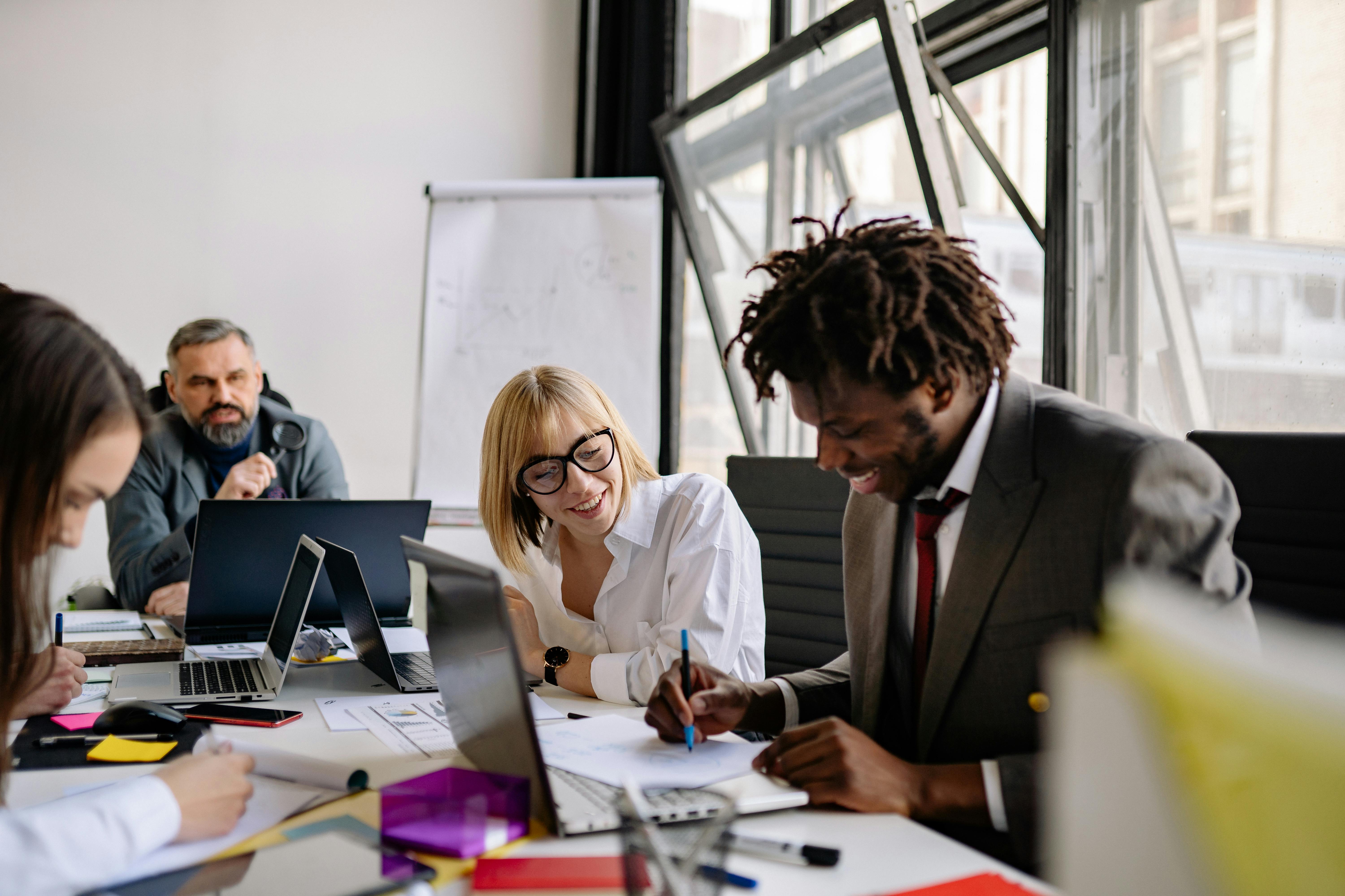 Diverse business professionals collaborating at a desk with laptops and documents in a bright office setting.