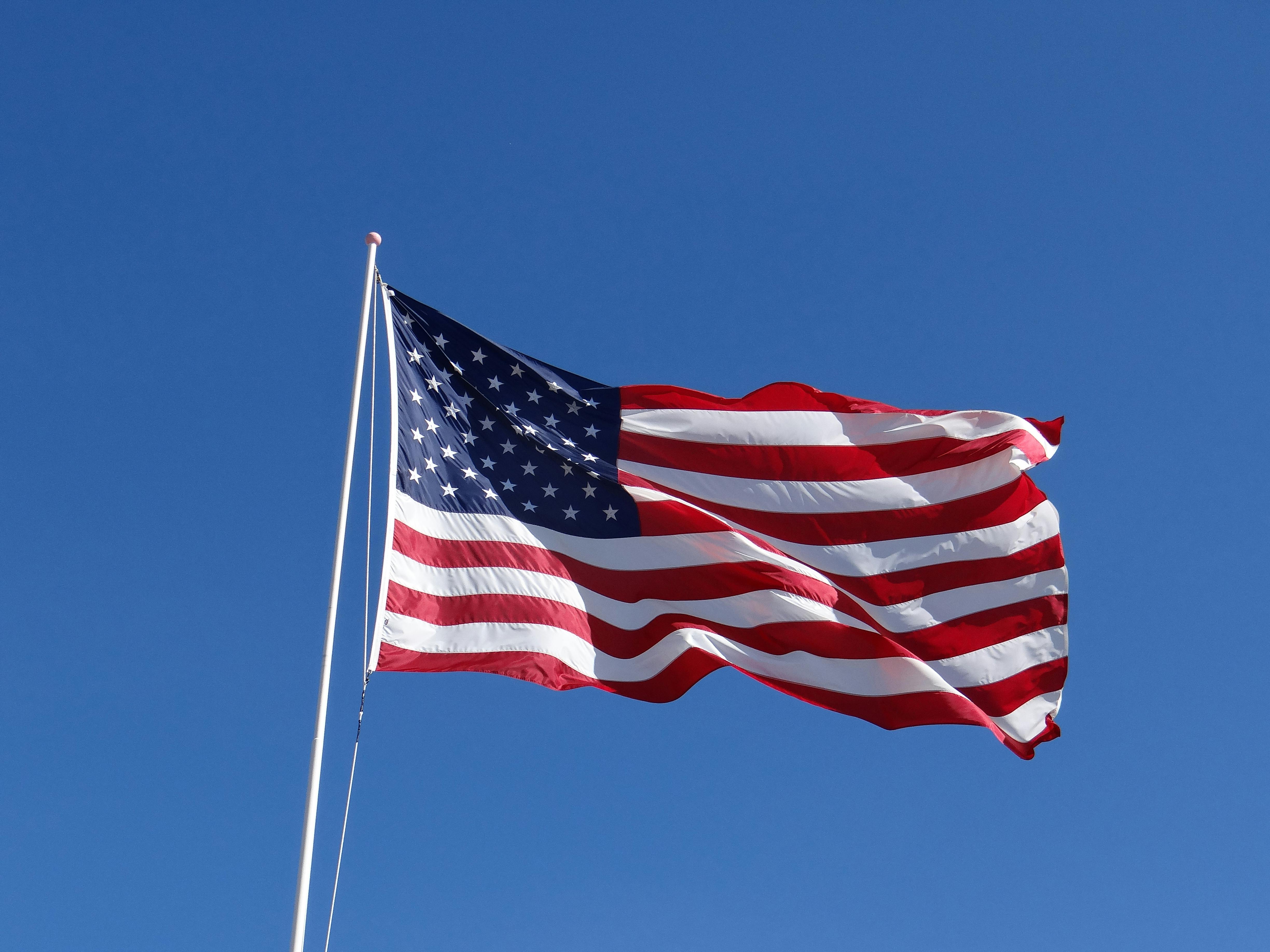 American flag waving on a flagpole against a clear blue sky.