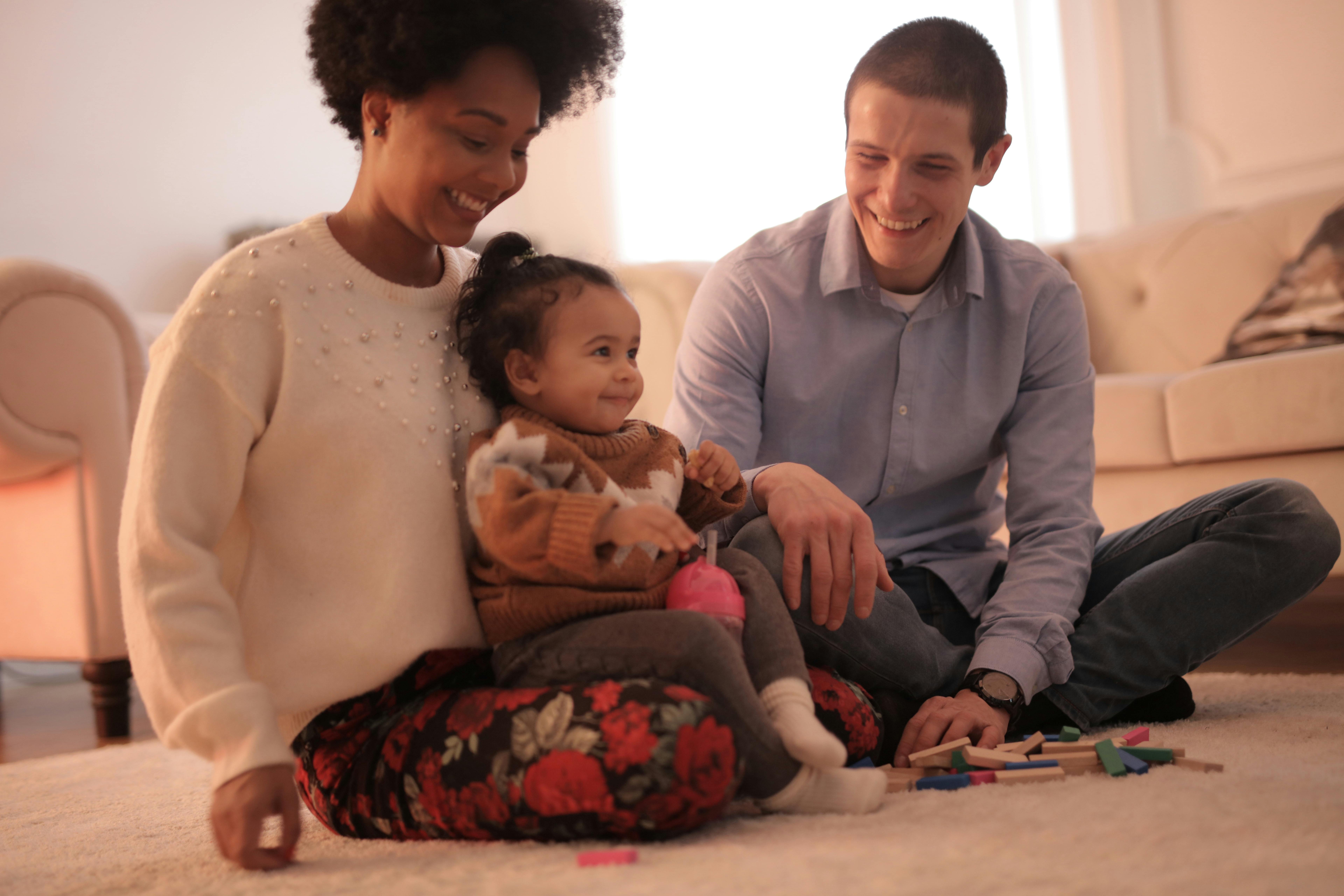 Two parents sitting on the floor with their young child, smiling and playing together in their home