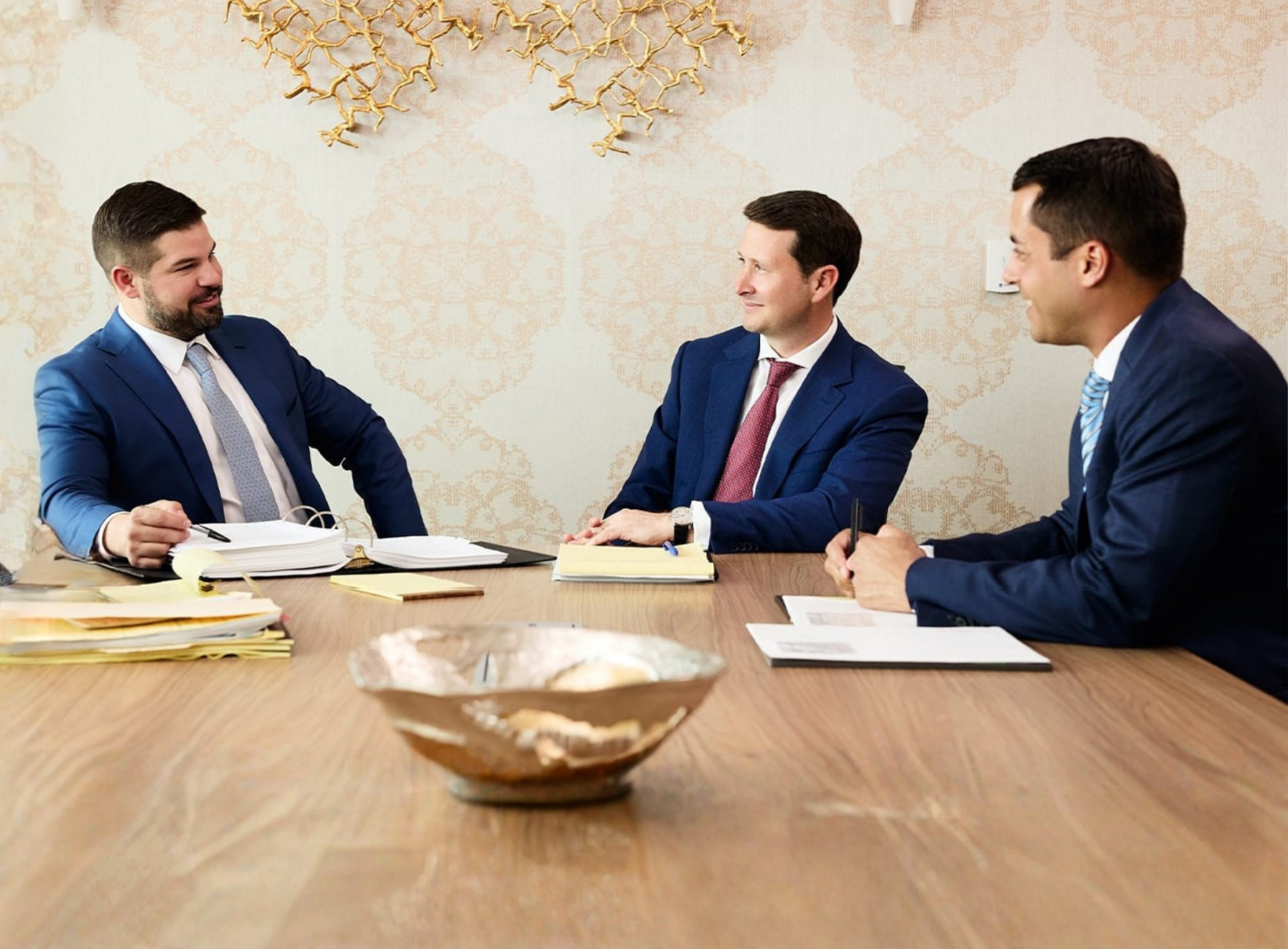 Three attorneys in suits meeting at a conference table, reviewing documents and discussing a case.