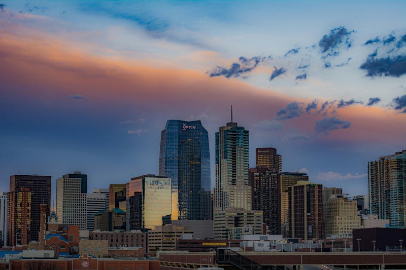 Denver, Colorado skyline at sunset with downtown office buildings and colorful clouds.