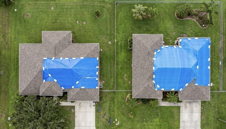 Aerial view of two residential homes with blue tarps covering roof damage after a hailstorm.