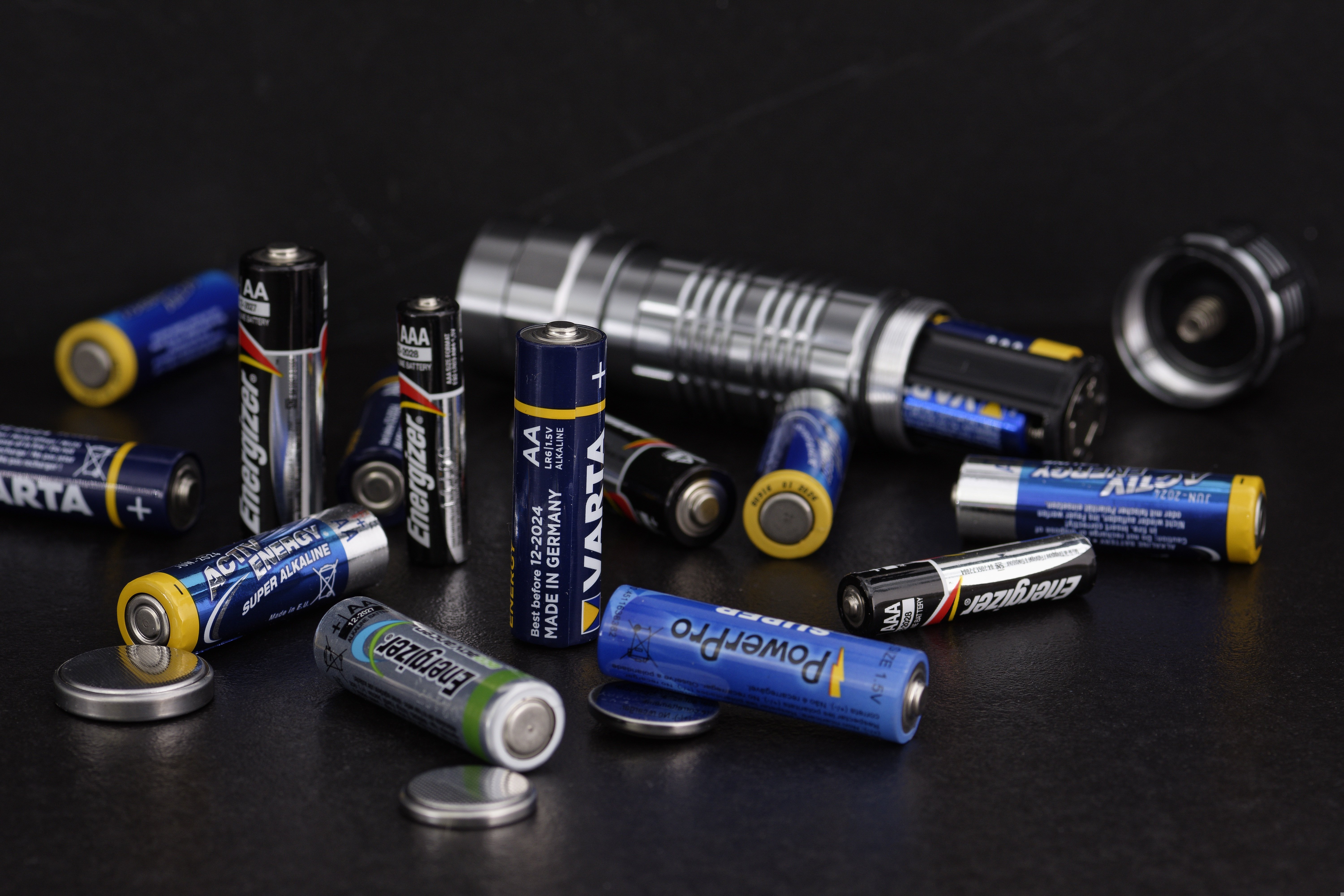 Different lithium-ion and rechargeable batteries placed next to a flashlight, showing the types of batteries that can create fire risks in homes and buildings.