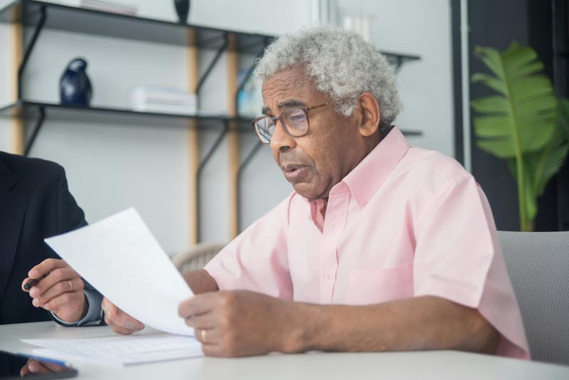 Senior man reviewing paperwork during a meeting, appearing concerned while reading documents related to a contract or financial agreement.